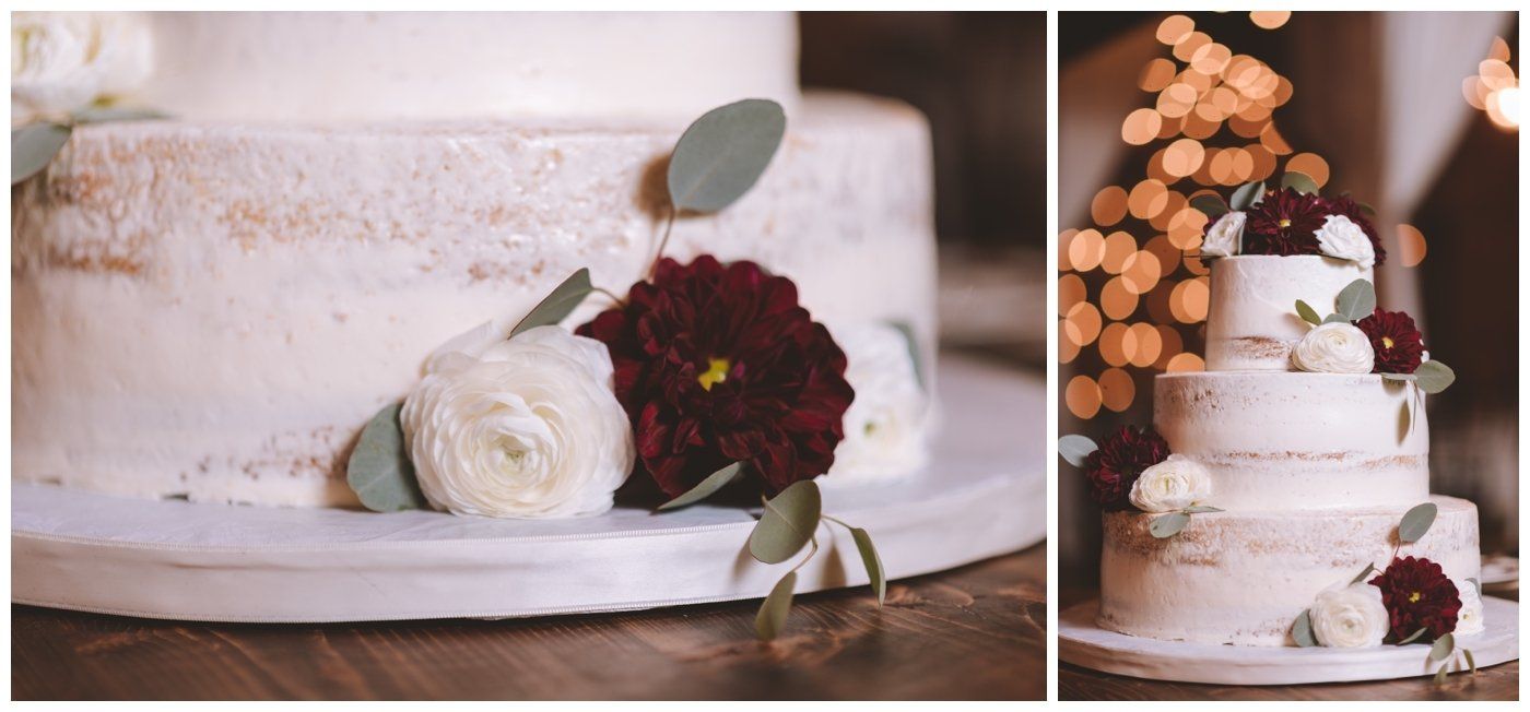 Elegant white wedding cake with flowers and burgundy accents on a dessert table.