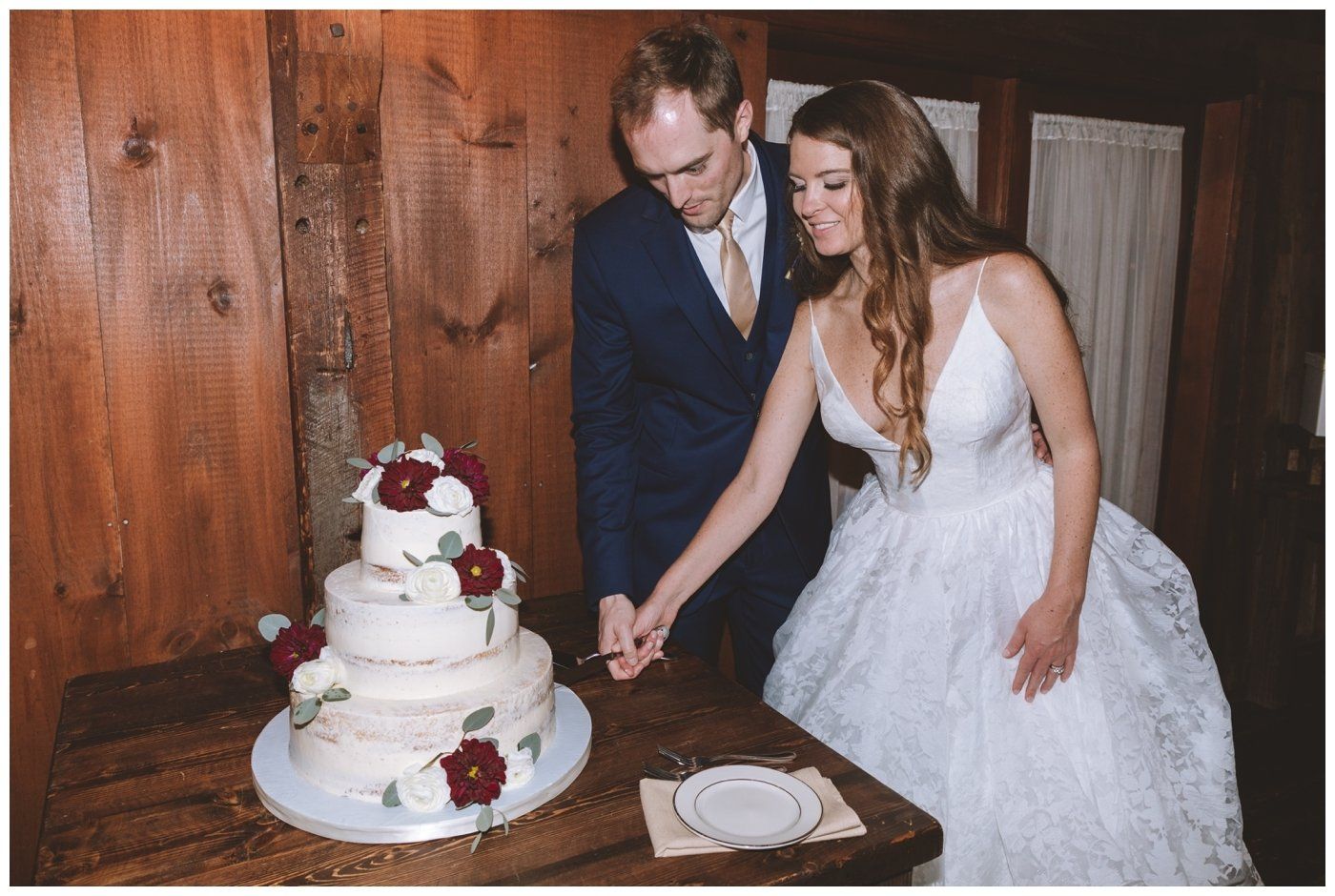 Bride and groom cutting a white wedding cake in a wood-paneled room