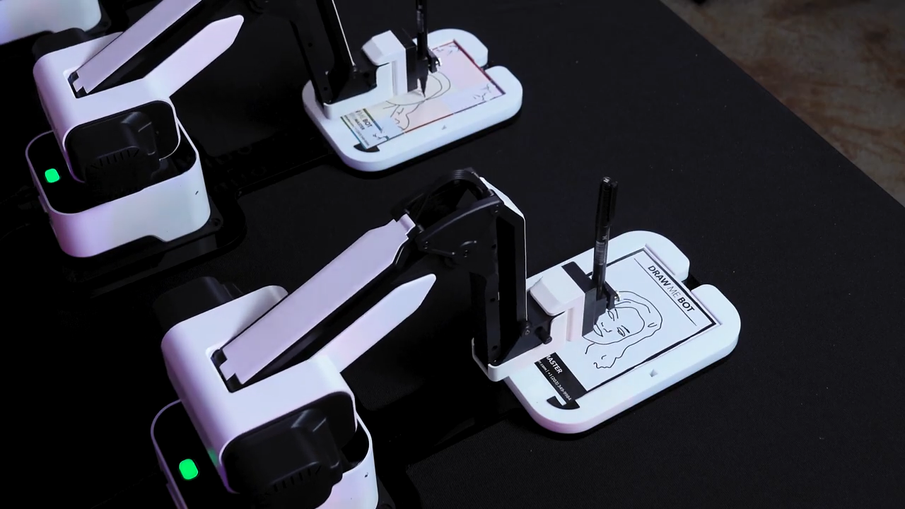 Three small robotic arms on a dark table, each mounted on a white base with green indicator lights.