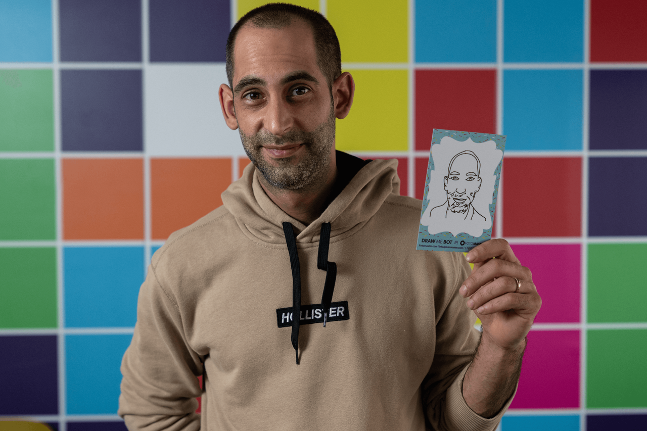 Man holding a small sketch card in front of a colorful tiled wall