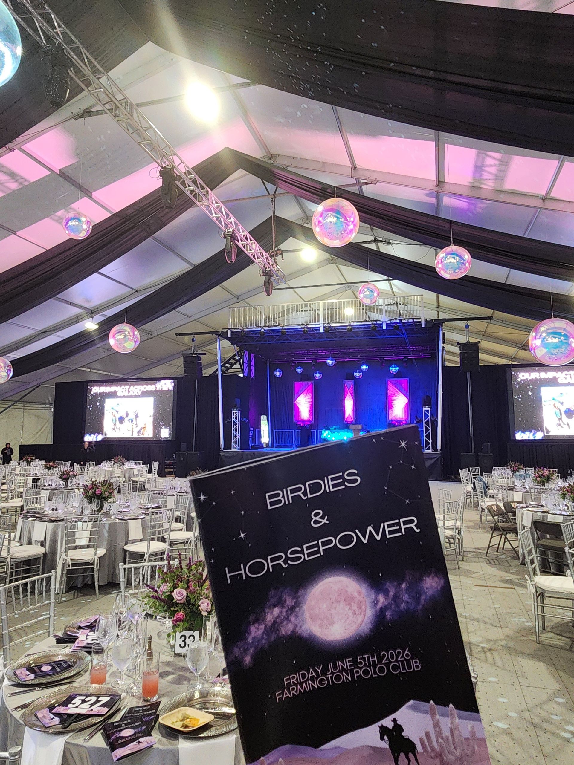 Banquet hall with stage lit purple and pink, tables set for guests, and a sign reading “Embrace & Empower.”