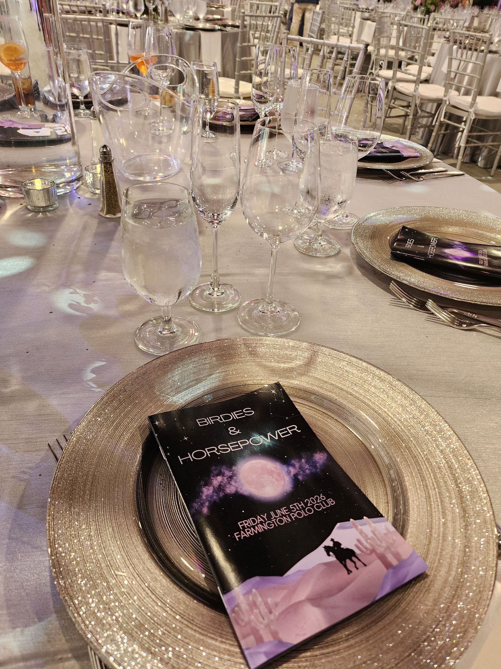 Elegant banquet table with silver chargers, glassware, and a purple-and-black menu card on a set place setting