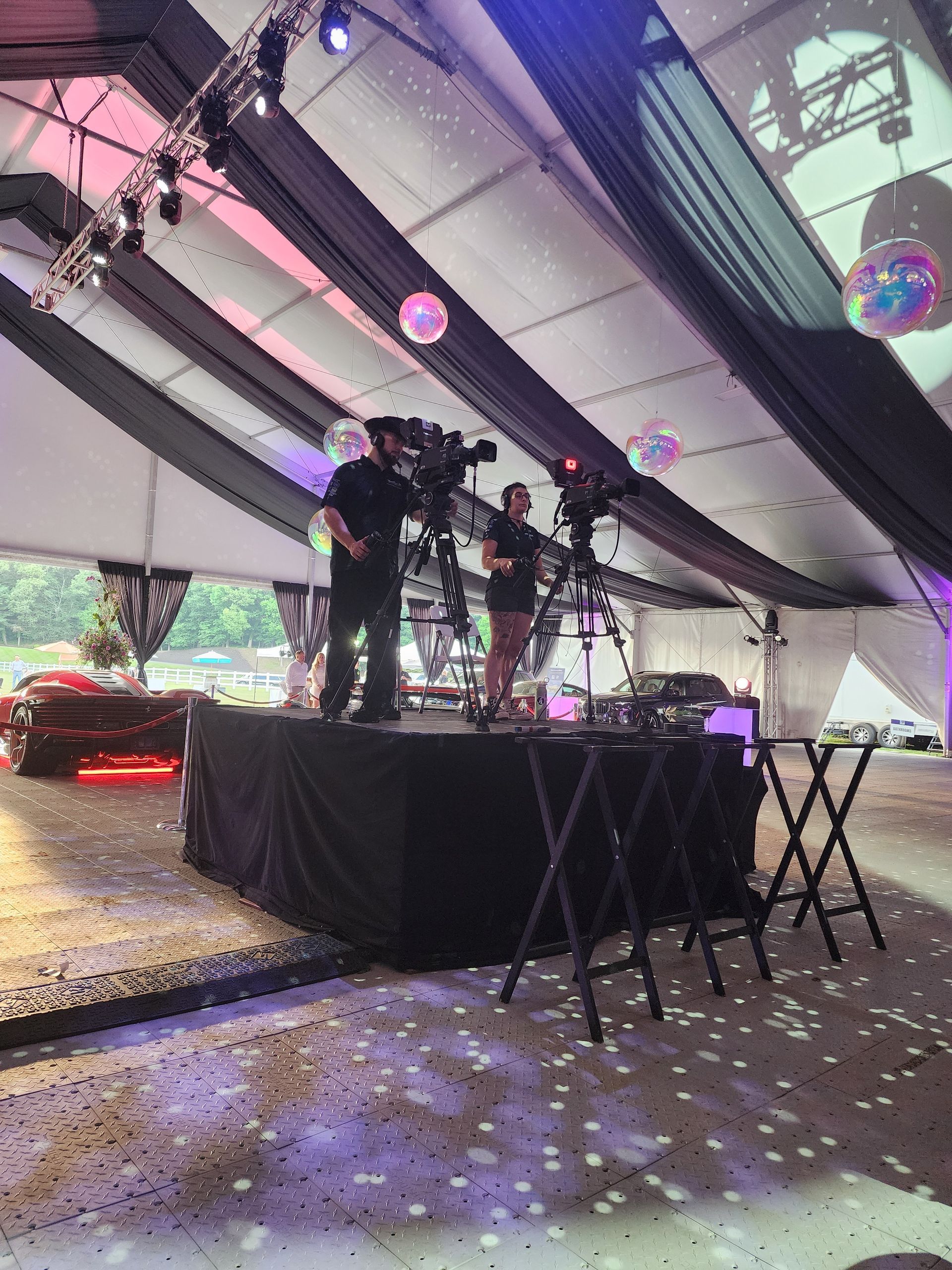 Three performers on a small stage under a tent, with disco balls and draped fabric overhead.