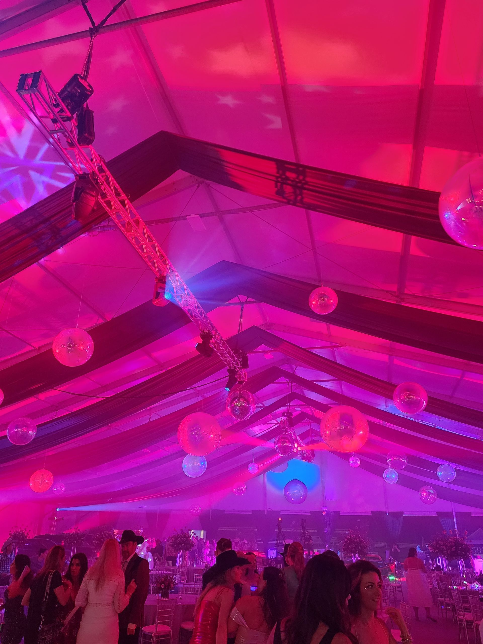 Crowded party tent glowing pink and purple with hanging decorations and people dancing beneath the roof