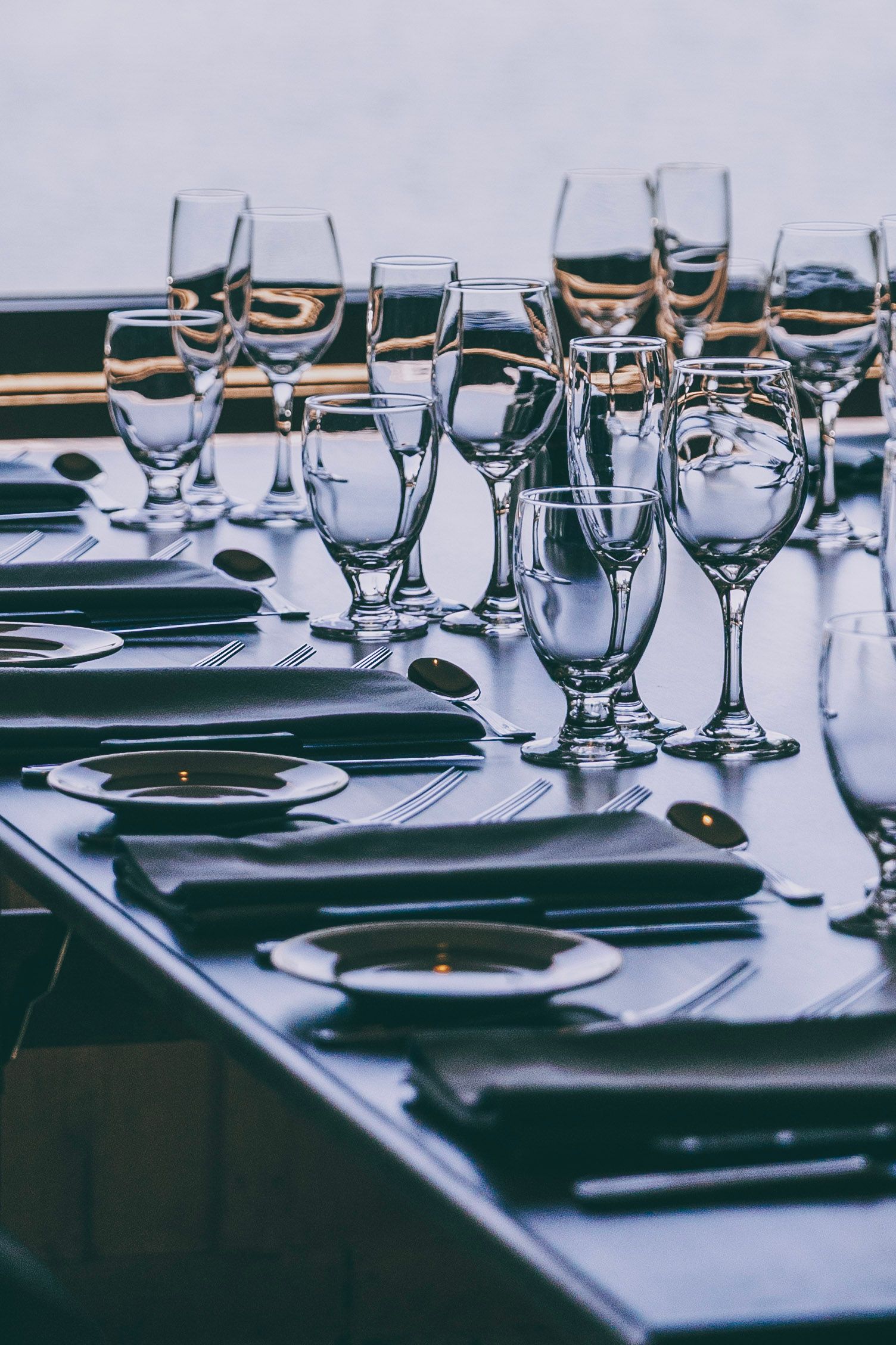 Set dining table with wine glasses, plates, and folded napkins in a dimly lit restaurant