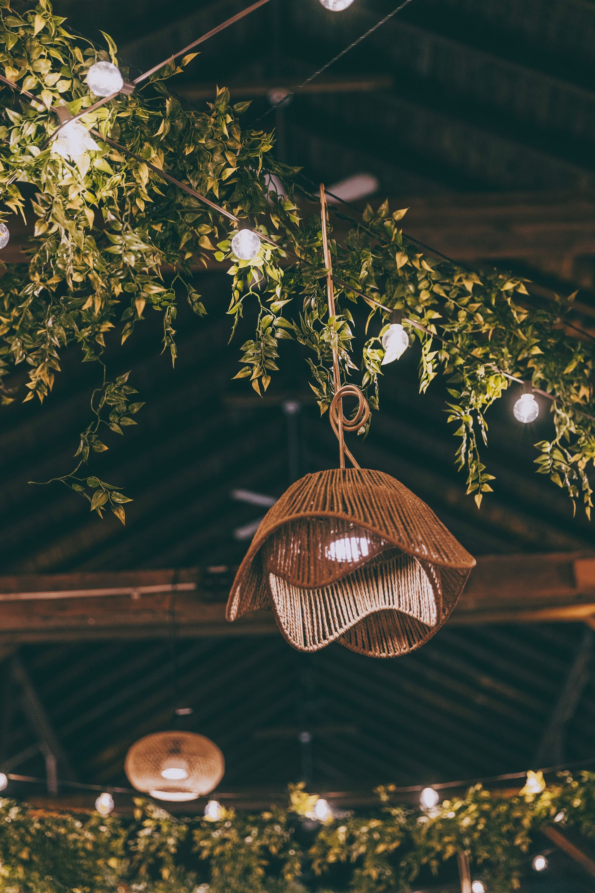Hanging woven lanterns and greenery lit by warm string lights in a rustic indoor venue