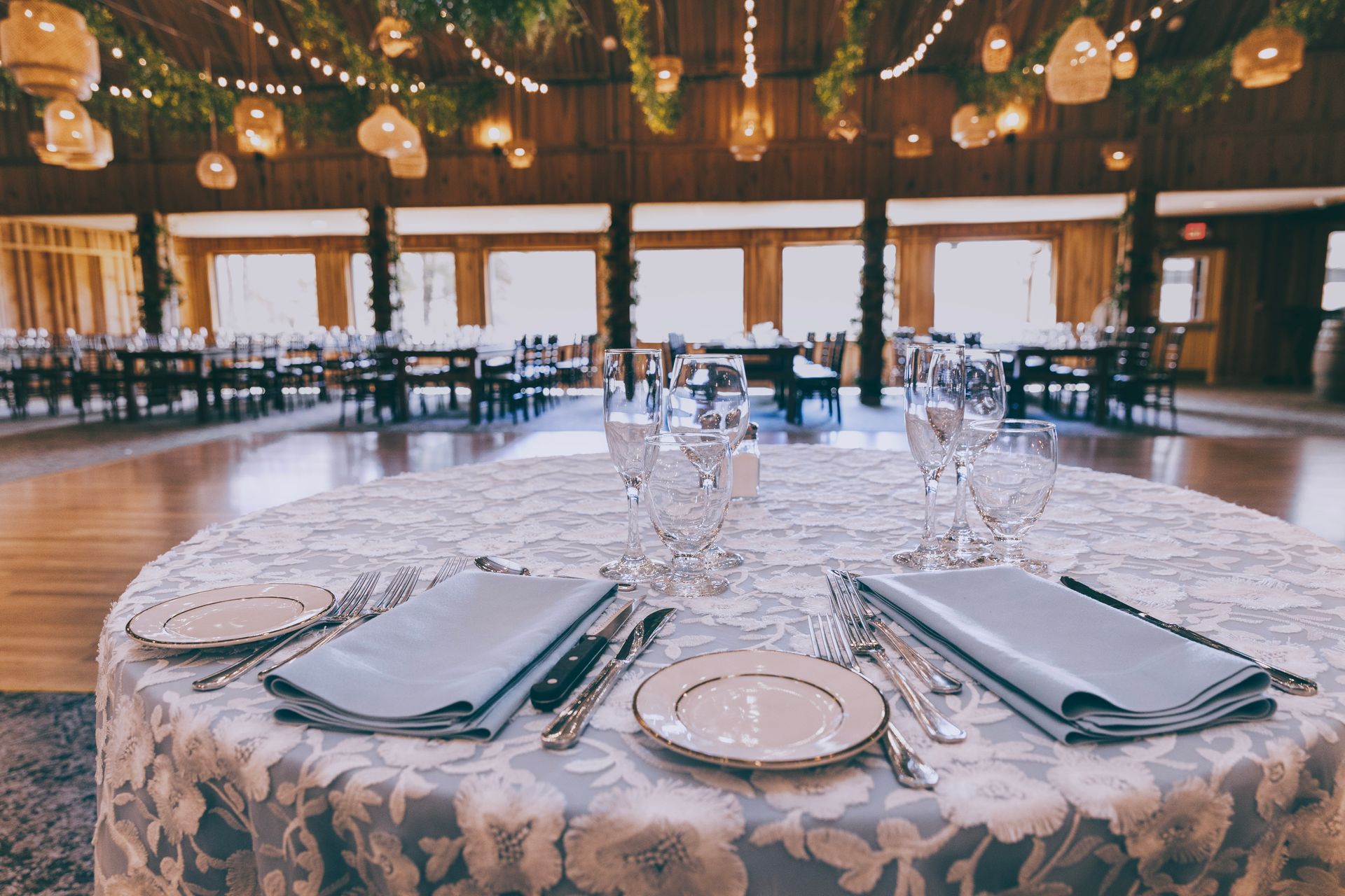 Set banquet table with plates, napkins, and glassware in a warmly lit reception hall