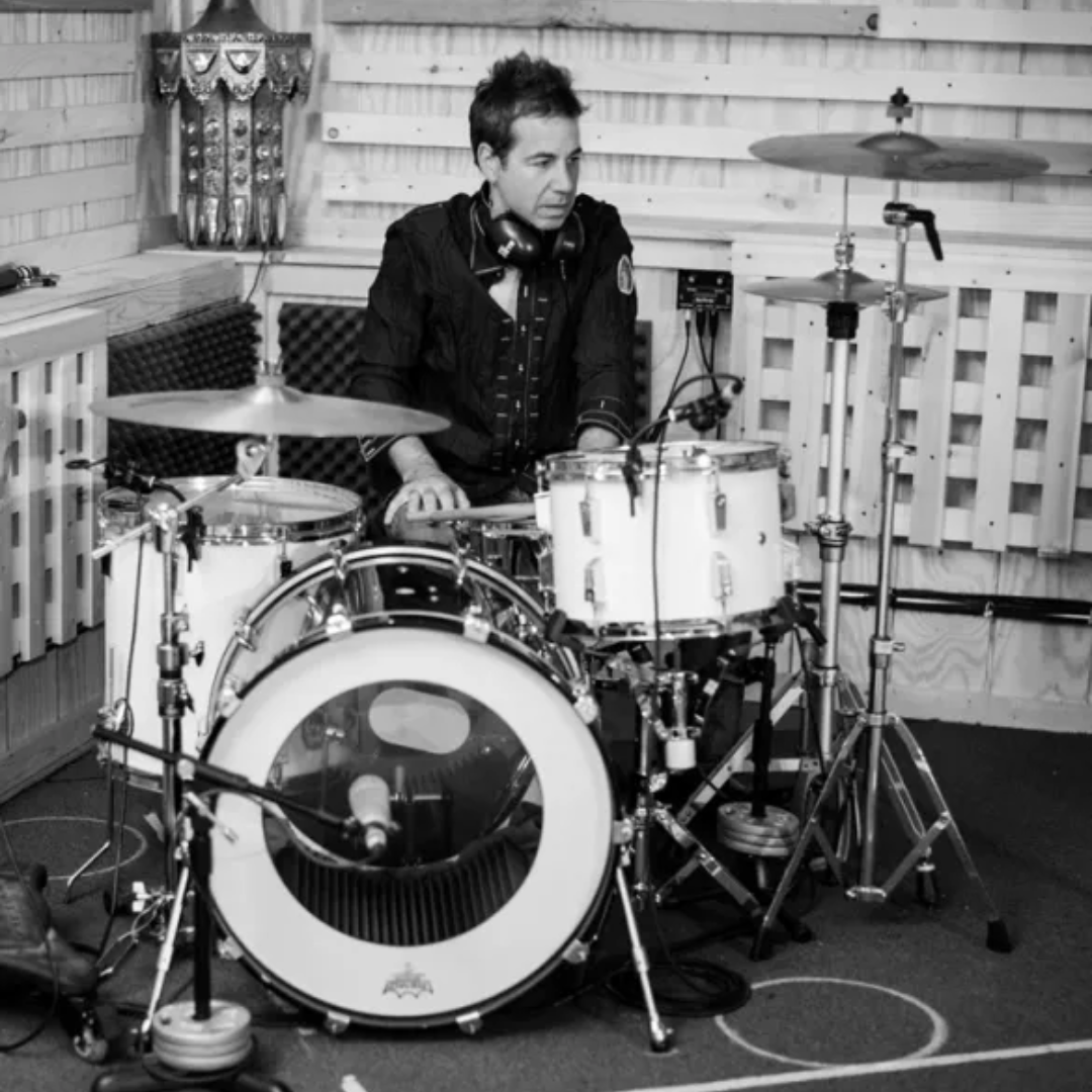 Drummer seated at a drum kit in a studio, looking to the side