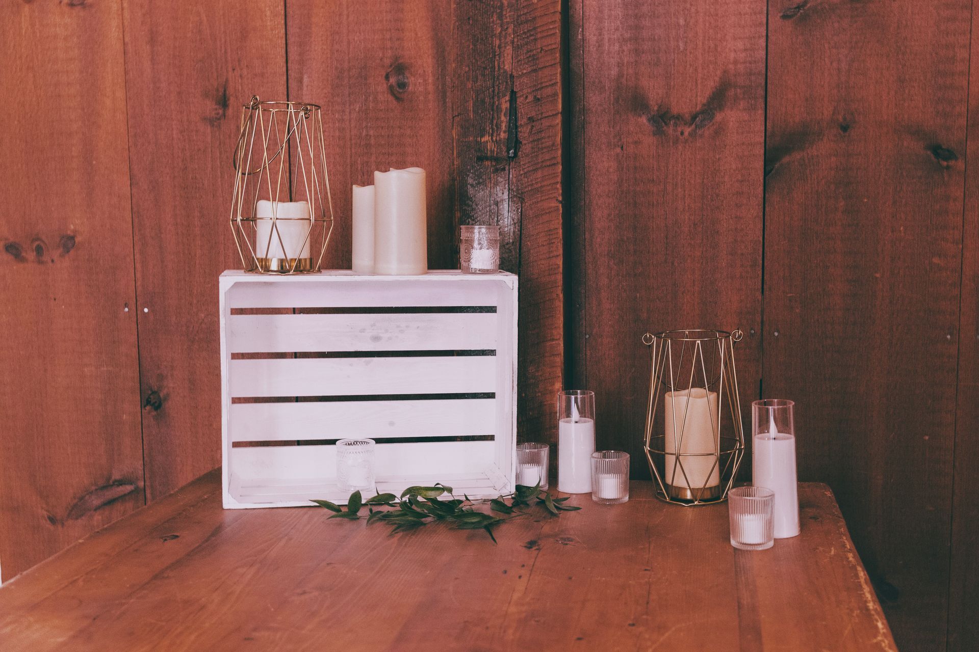 Rustic wooden tabletop with a white crate, candles, and small decorative jars against a red wood wall