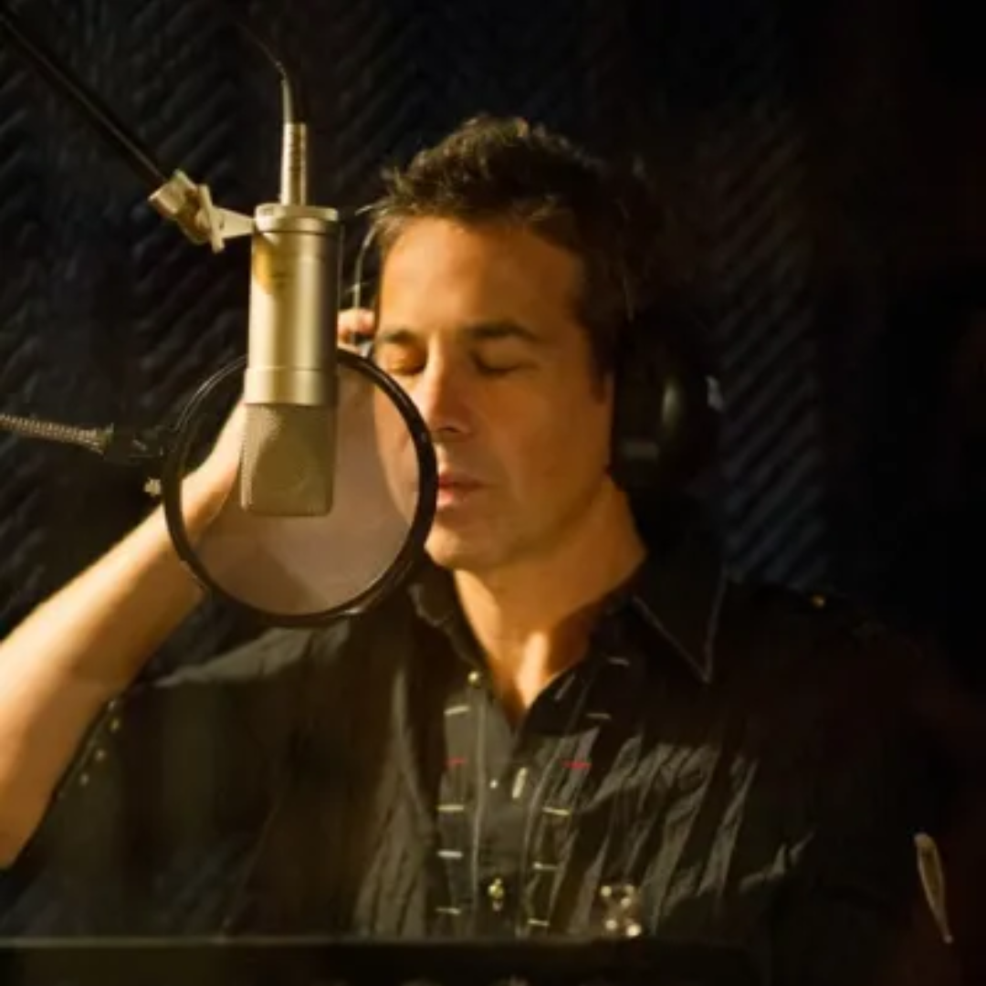 Singer in a recording studio, eyes closed, standing behind a microphone and pop filter.