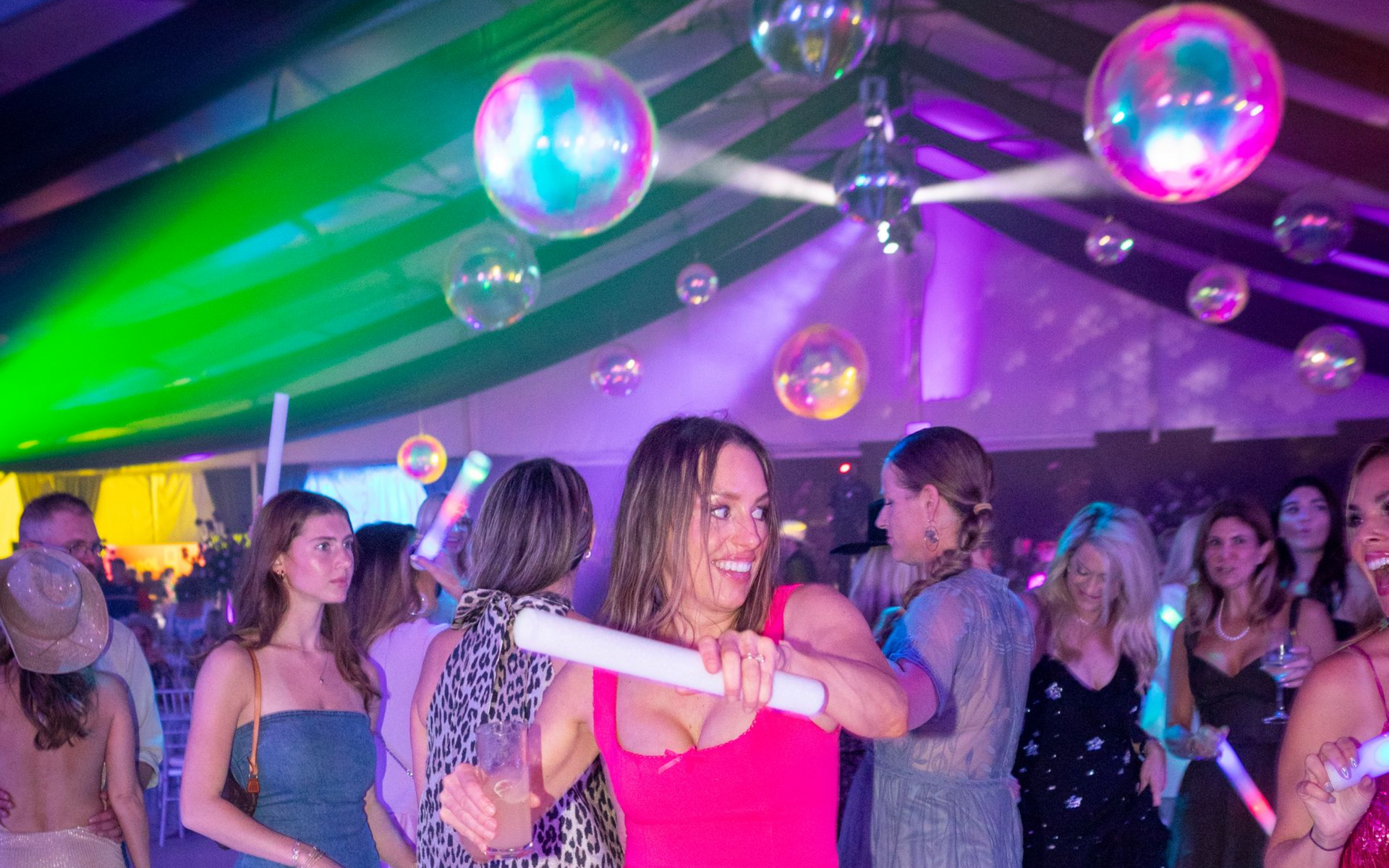 People dancing at a neon-lit party under green and purple lights with floating bubbles