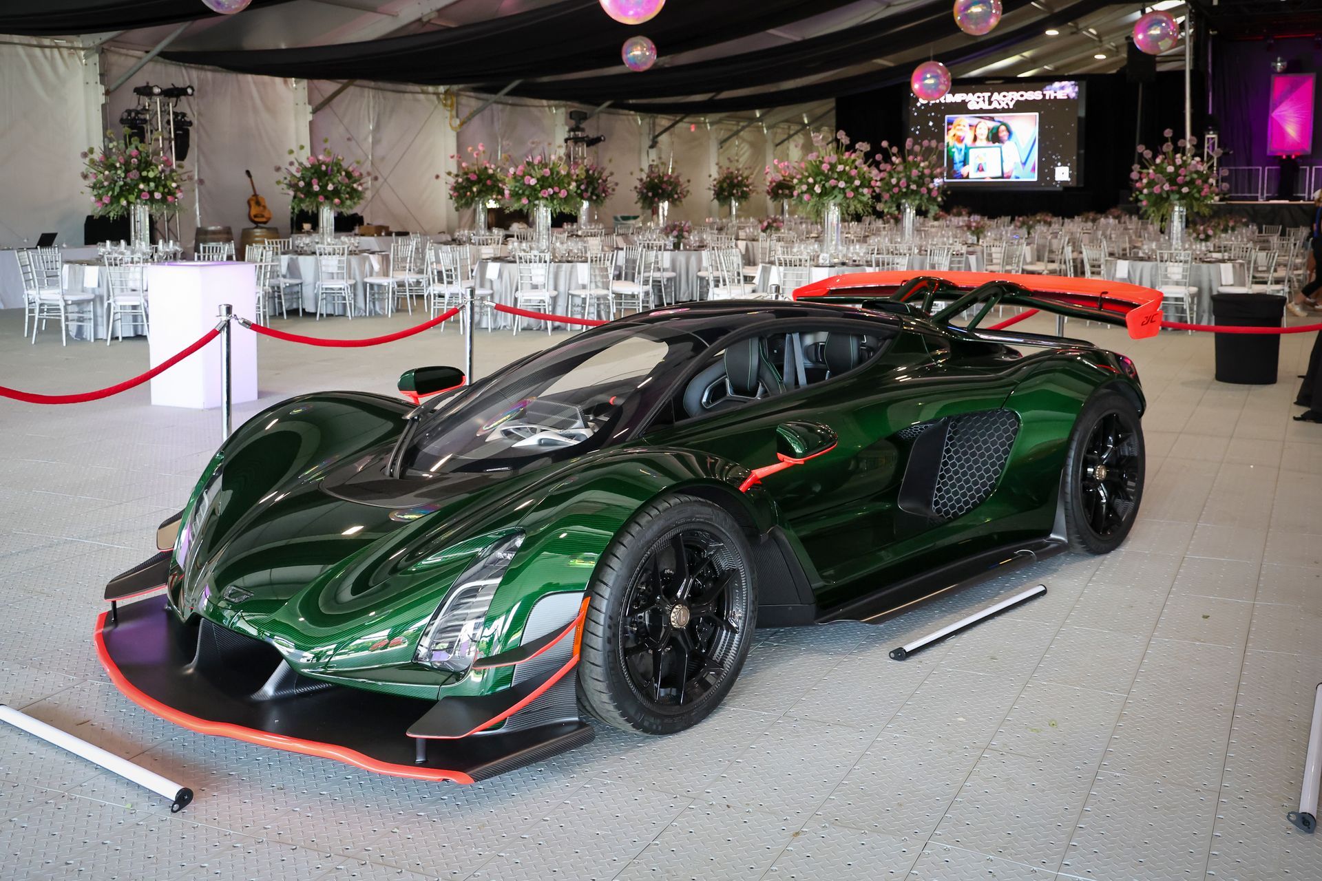 Dark green sports car on display indoors, surrounded by red ropes in a showroom-like venue.