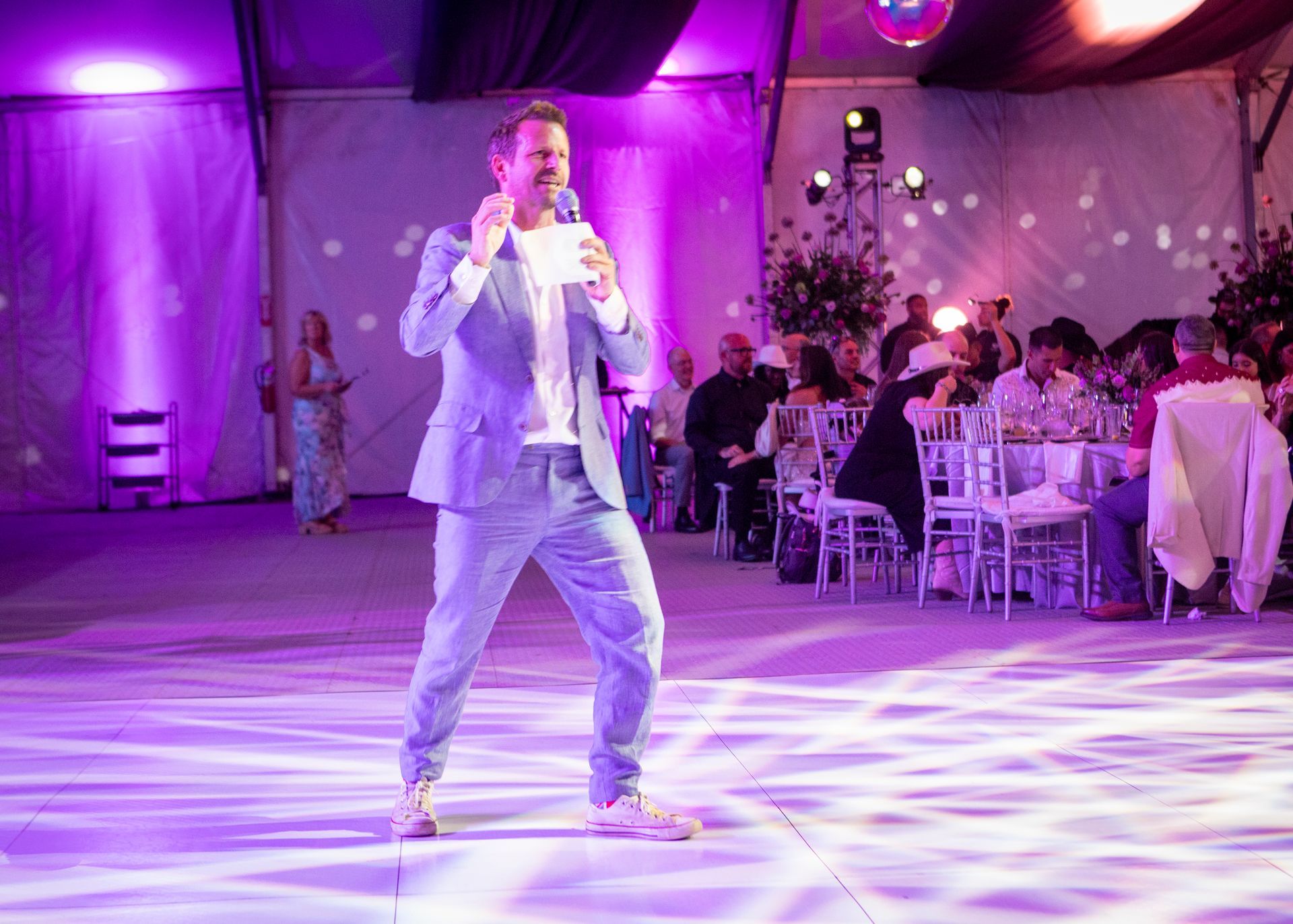 Singer performing on a lit dance floor at a purple-lit banquet hall event