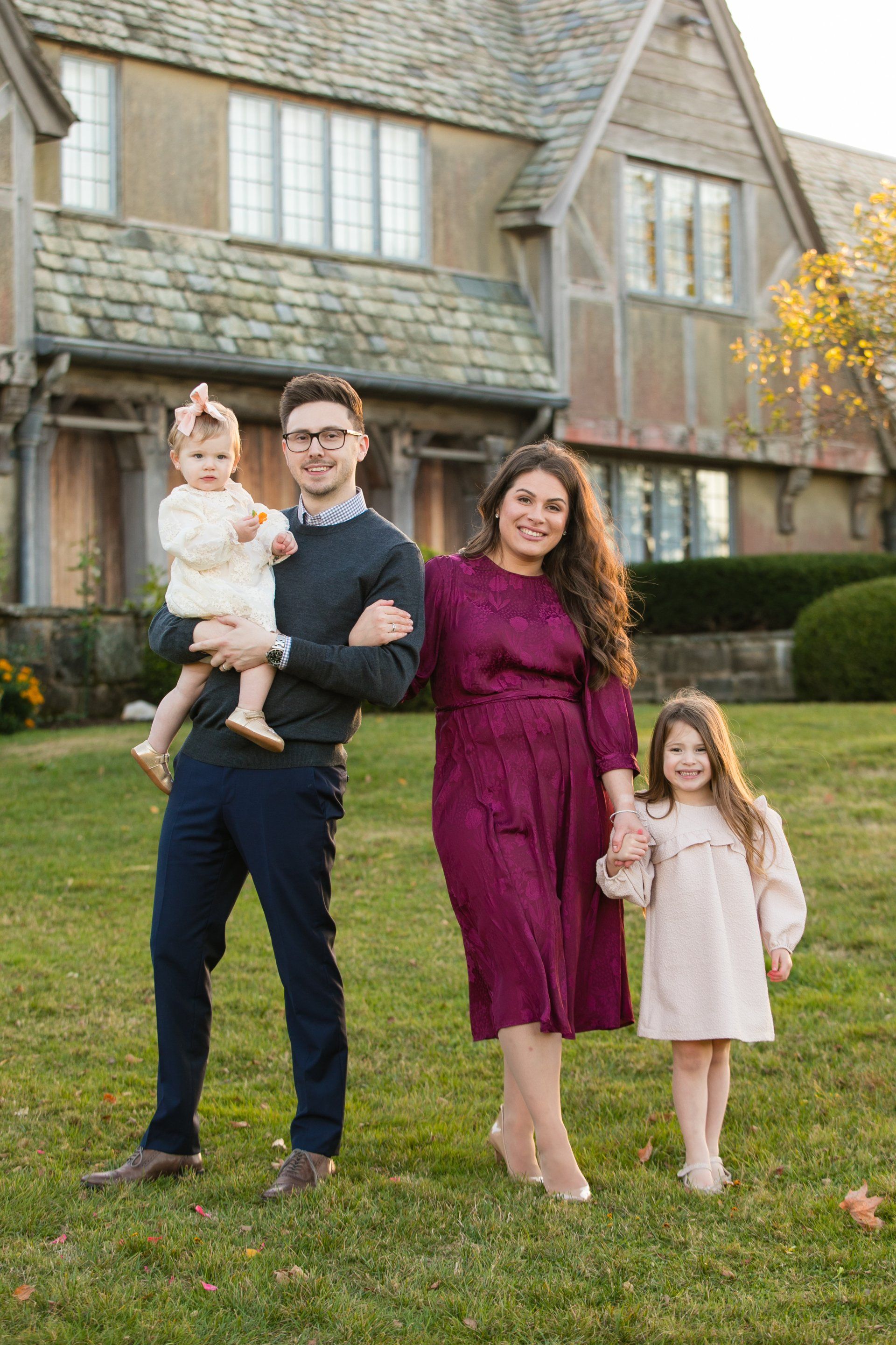 Family of four standing on a lawn in front of a house, dressed in formal outfits.