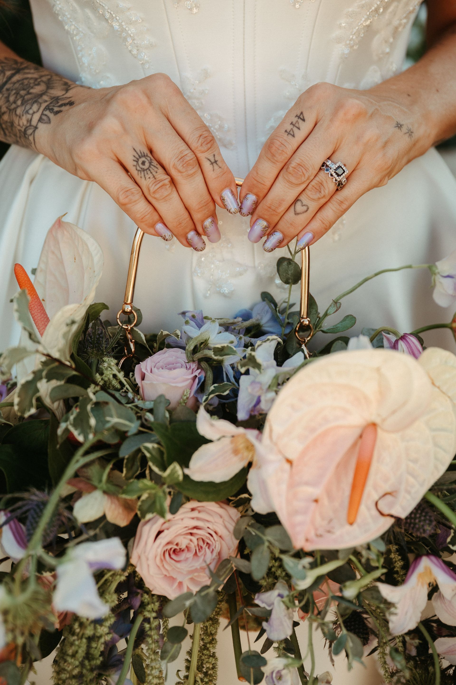 Hands with rings holding a bouquet of pastel roses and greenery in a white dress