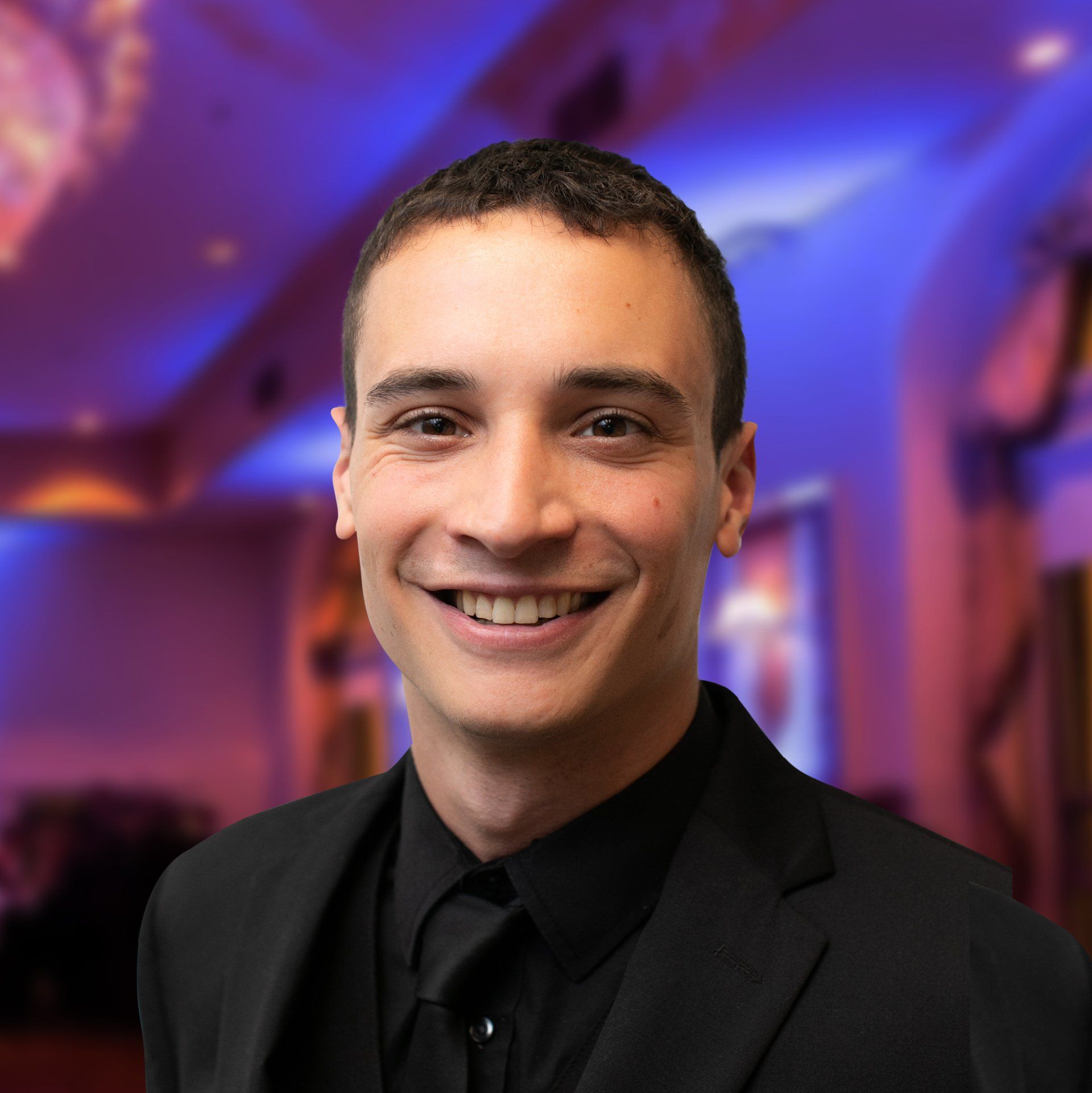 Smiling man in a dark suit and tie at a decorated indoor event.