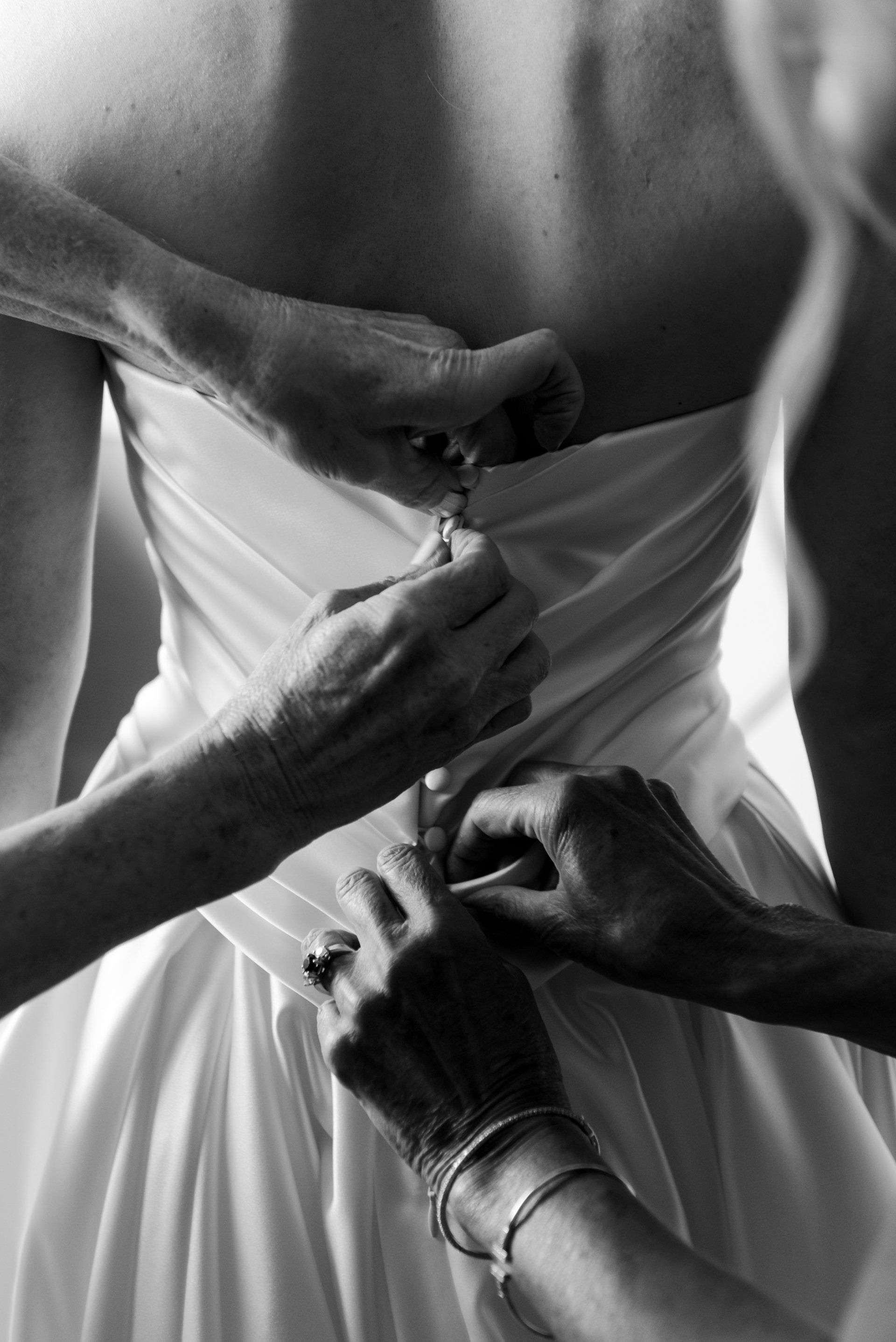 Hands fastening the back of a white dress with a zipper and buttons