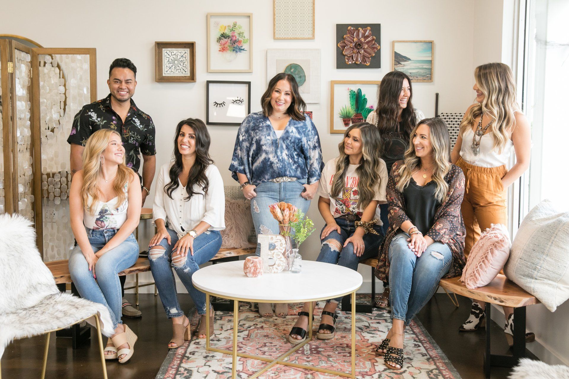 Group of people posing in a bright living room with framed art, plants, and a round coffee table.