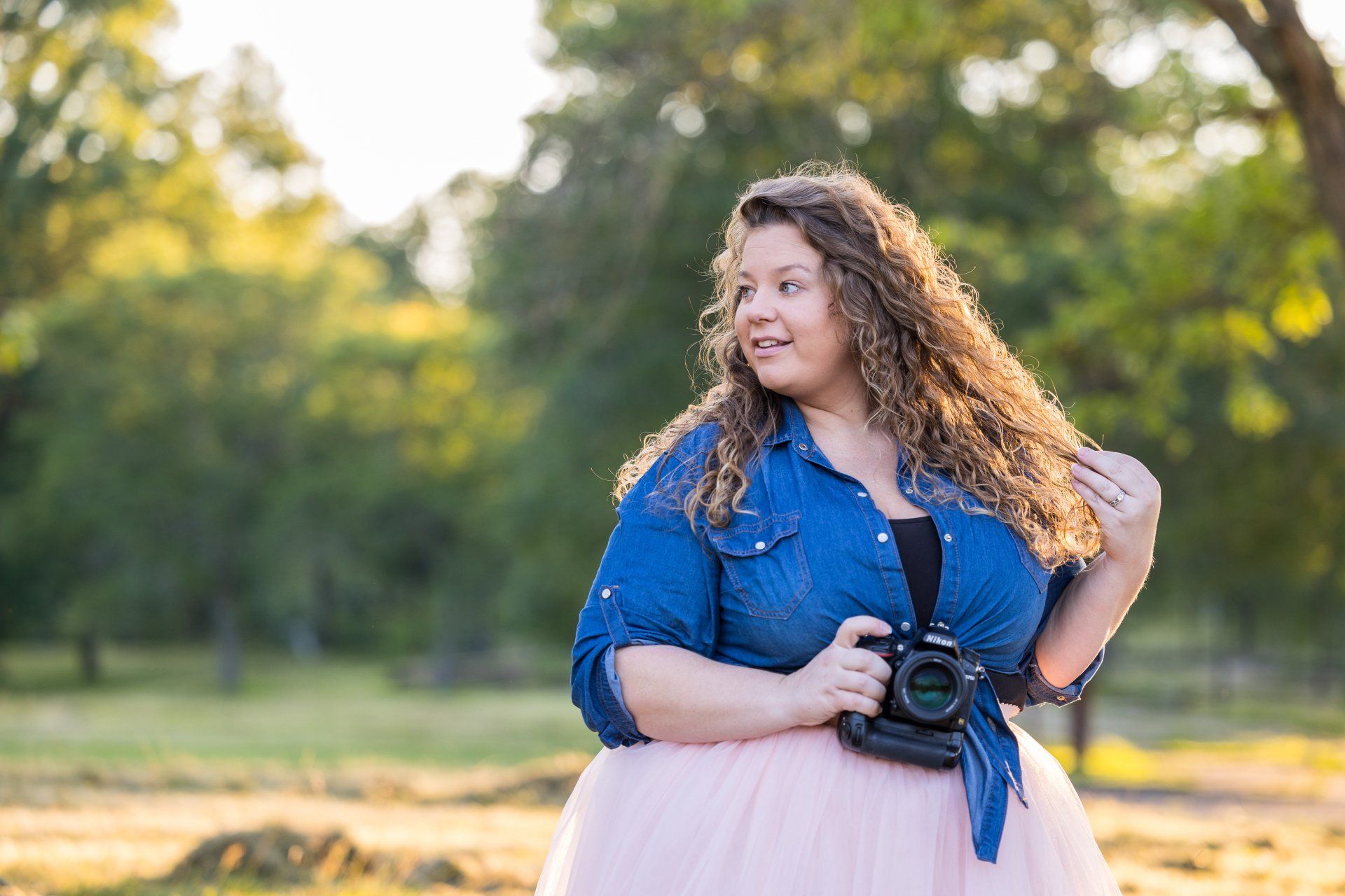 Woman in a blue shirt and pink skirt holding a camera in a sunlit park