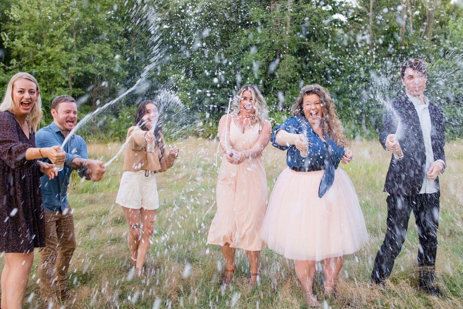 Wedding party celebrating outdoors with champagne spray in a grassy field