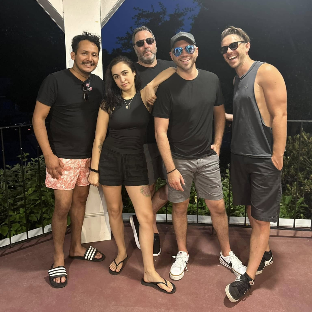 Five friends posing together outdoors at night, smiling and dressed casually.