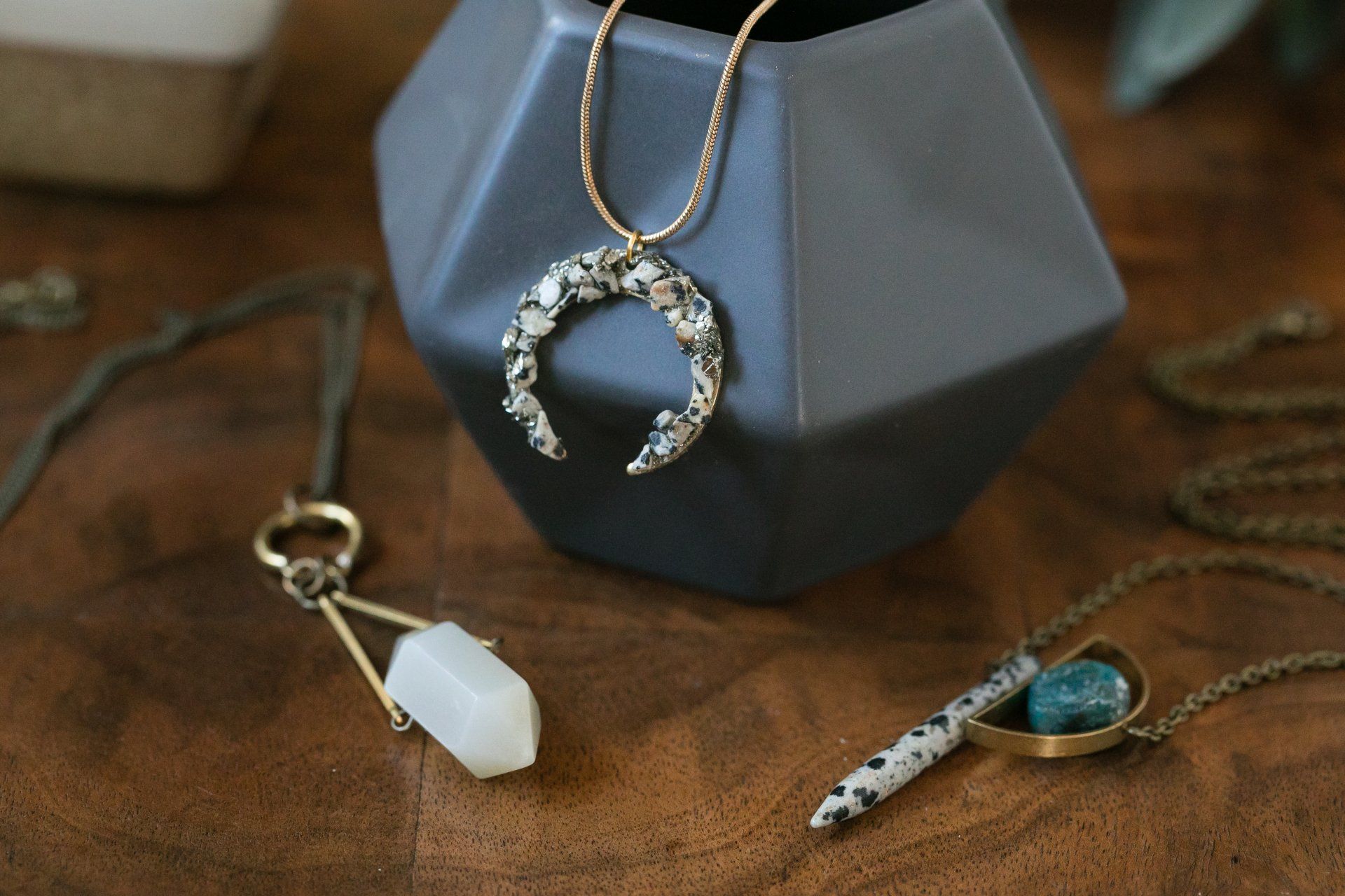 Assorted necklaces and pendants on a wooden surface, including a crescent moon and white crystal charm.