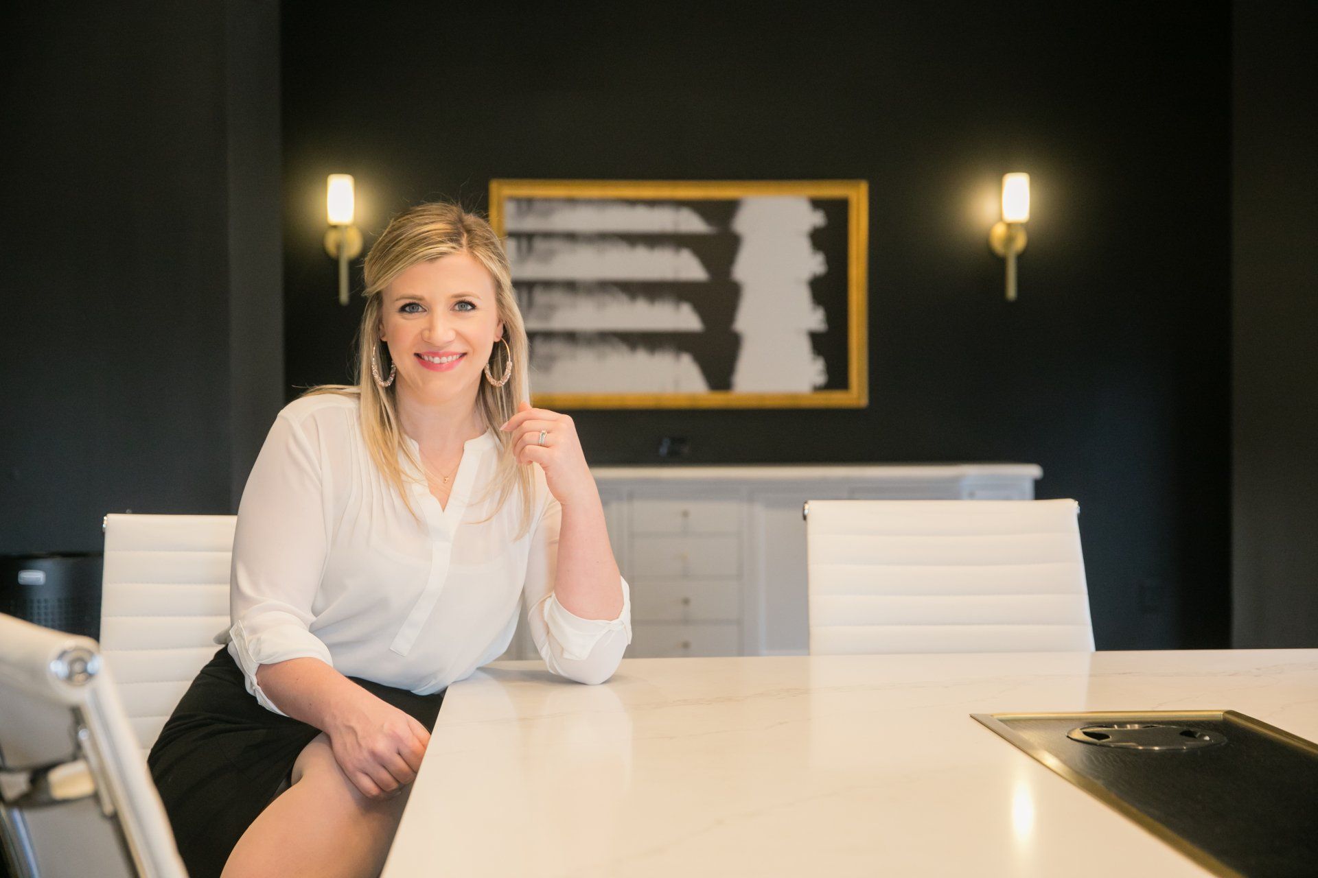 Woman seated at a conference table in a modern office, smiling and holding a pen