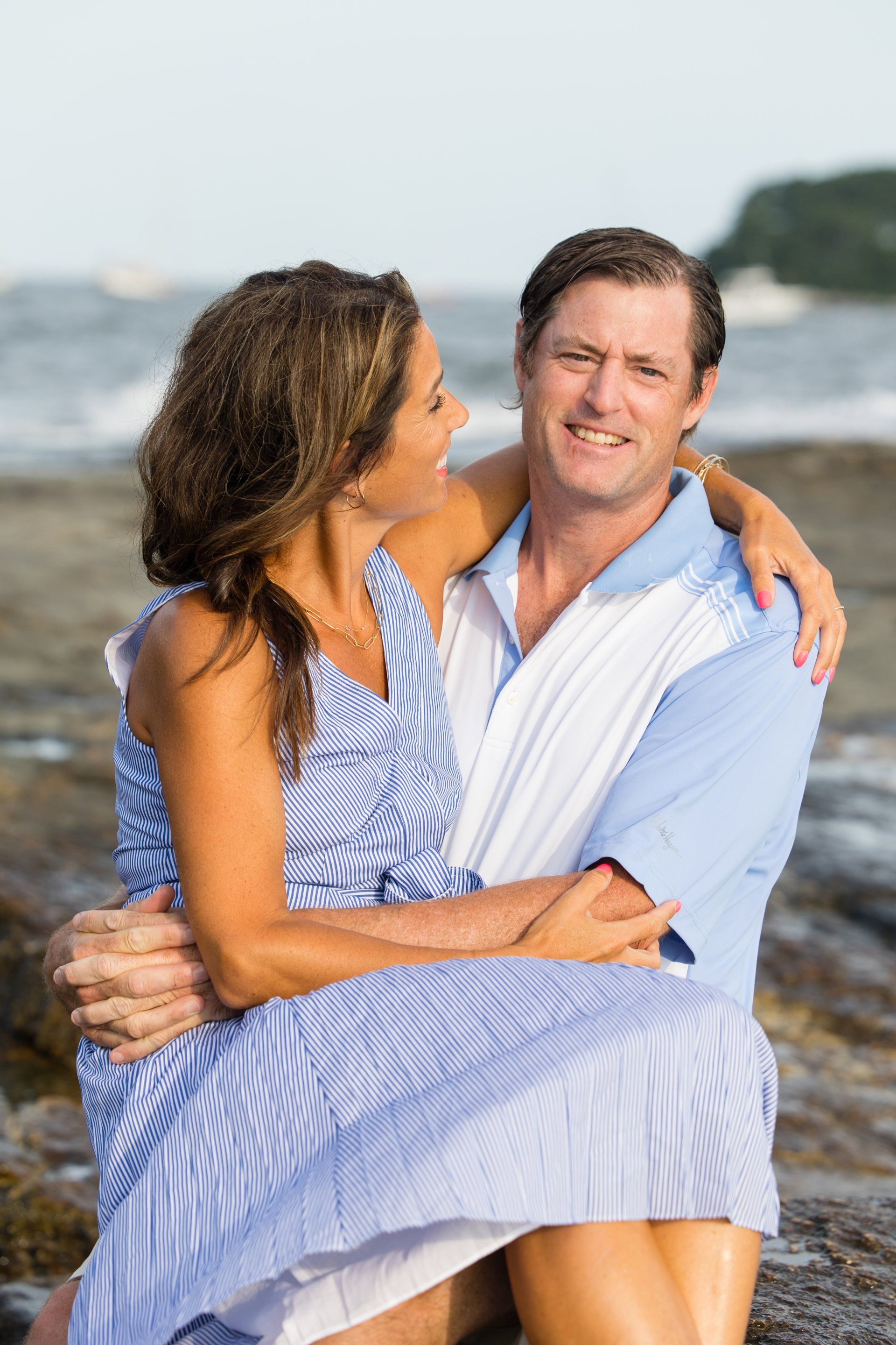 Couple embracing on a beach, with the woman in a blue patterned dress and the man in a white shirt.