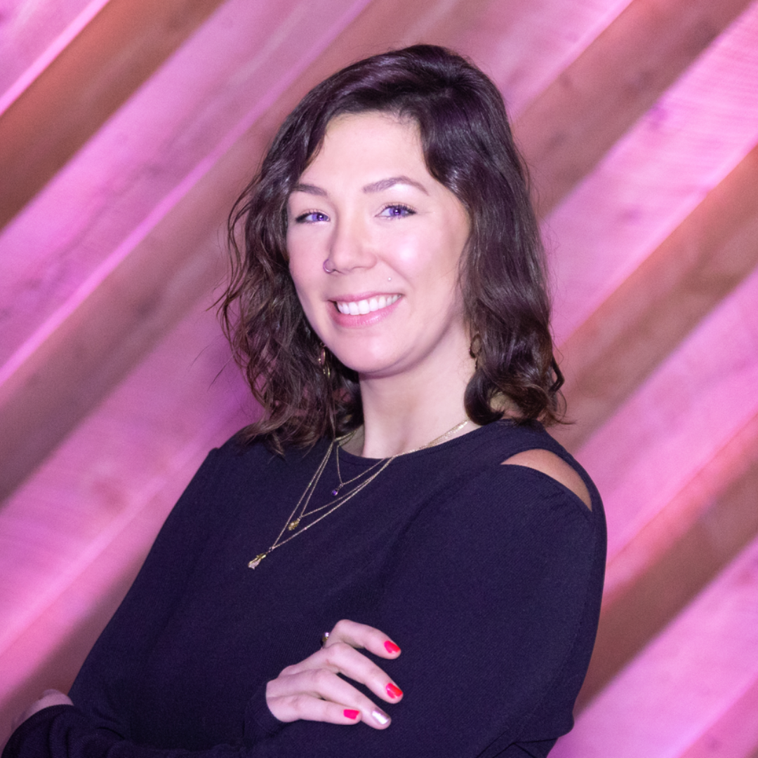 Smiling person in a black top with gold necklaces against a diagonally striped background