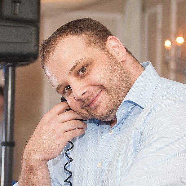 Man in a light blue shirt smiling while holding a DJ headphone indoors