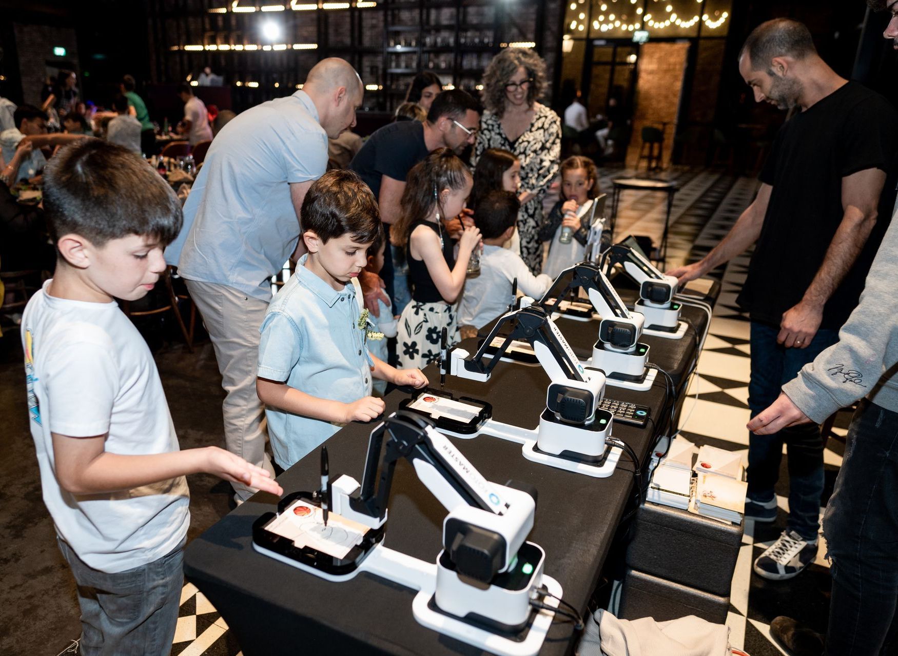 People examining robotic arms on a table in a dimly lit workshop or exhibit space