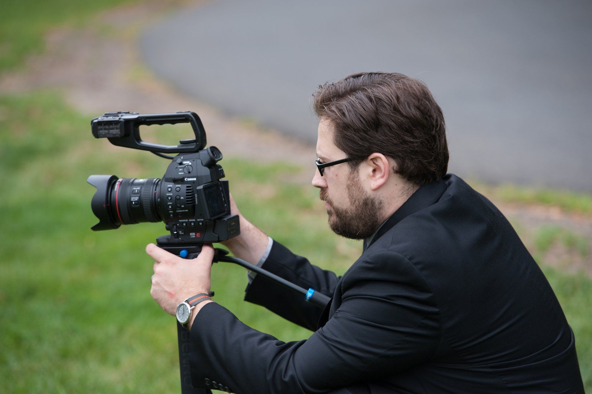 Photographer crouching outdoors, aiming a DSLR camera with a mounted microphone.