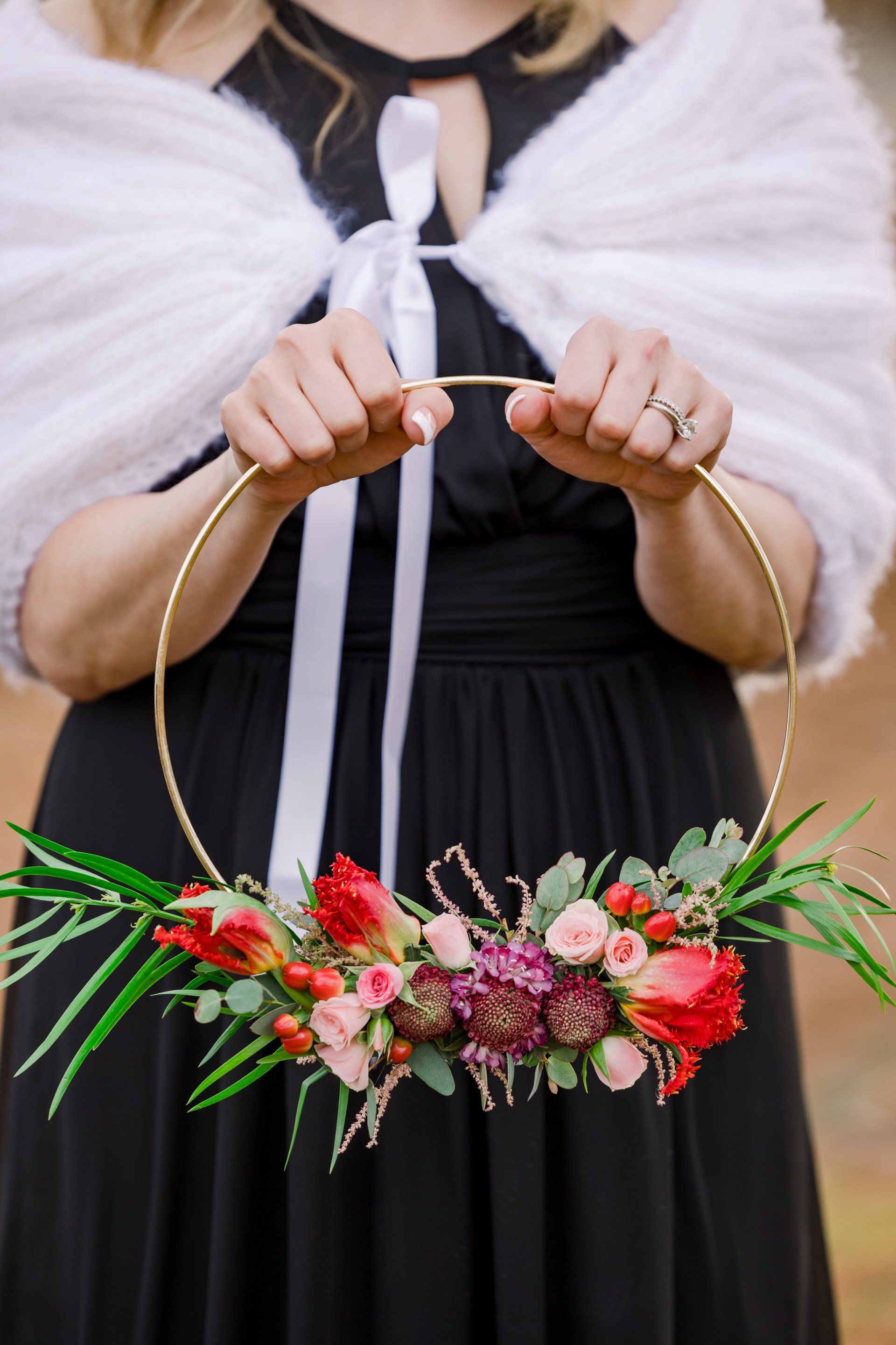 Person in a black dress holding a floral hoop bouquet with red, pink, and white flowers