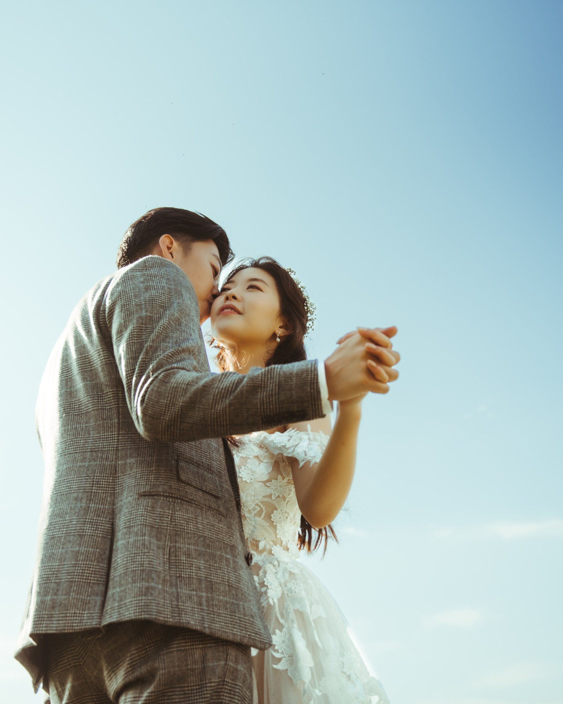 Couple dancing outdoors under a bright blue sky, holding hands and facing each other