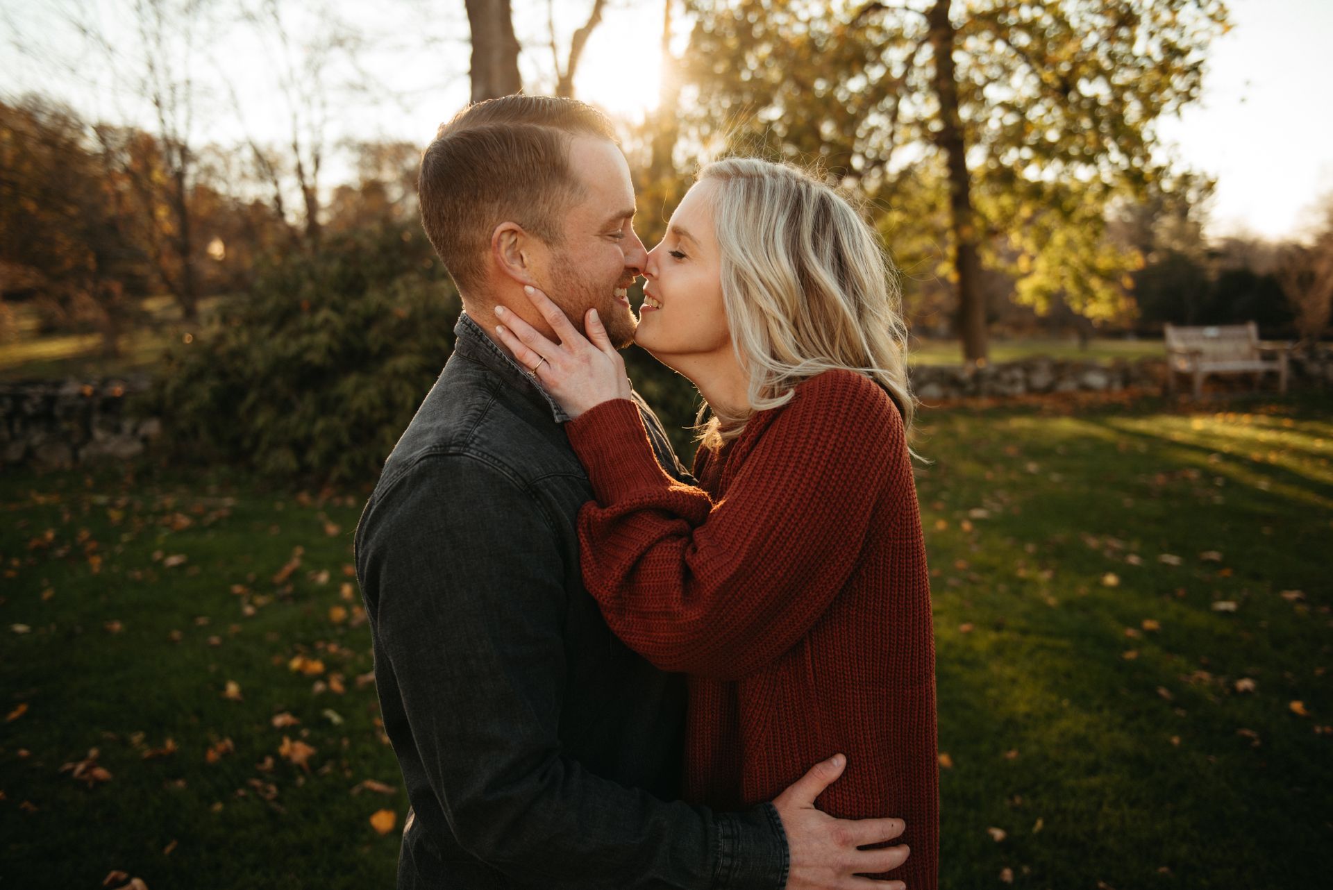 Couple embracing and kissing outdoors in a sunlit park during autumn