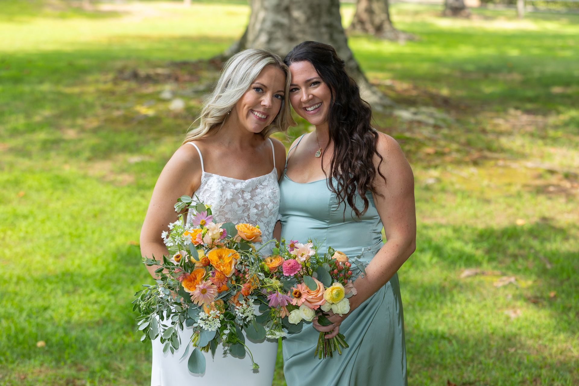 Two women in dresses holding colorful bouquets on a sunny lawn