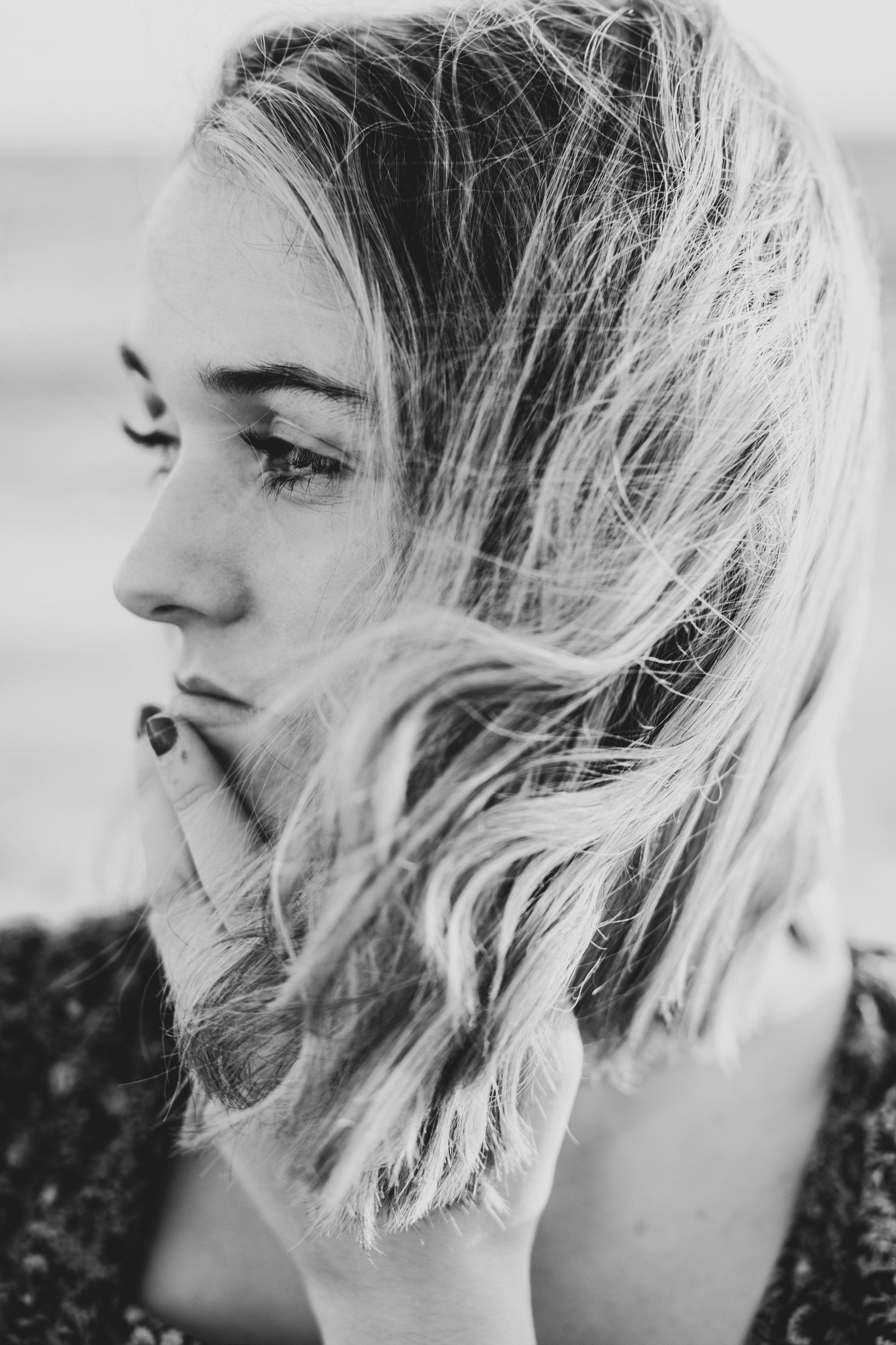 Black-and-white profile portrait of a person with windblown hair, looking left outdoors