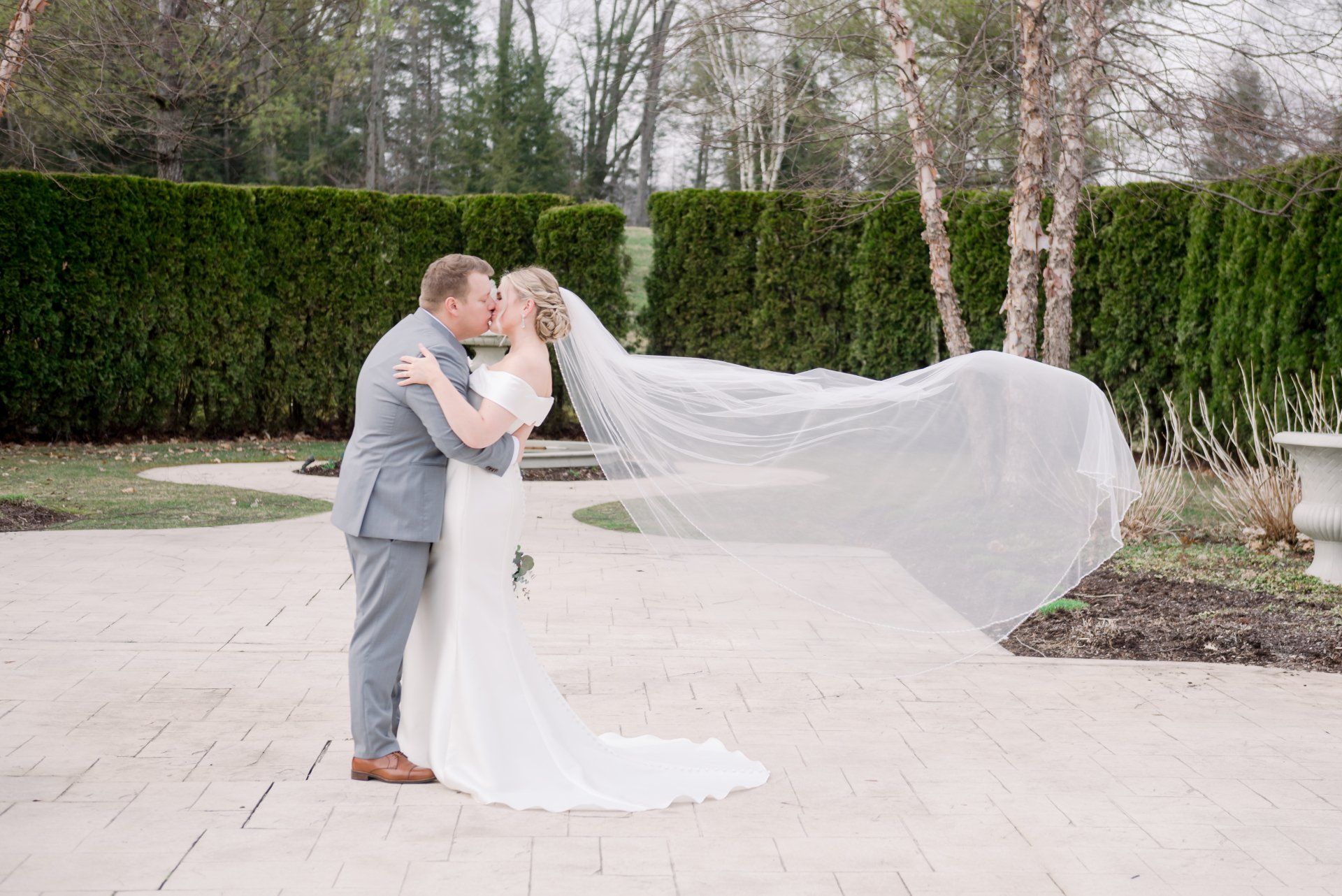Bride and groom kiss in a garden, her long veil flowing behind them.