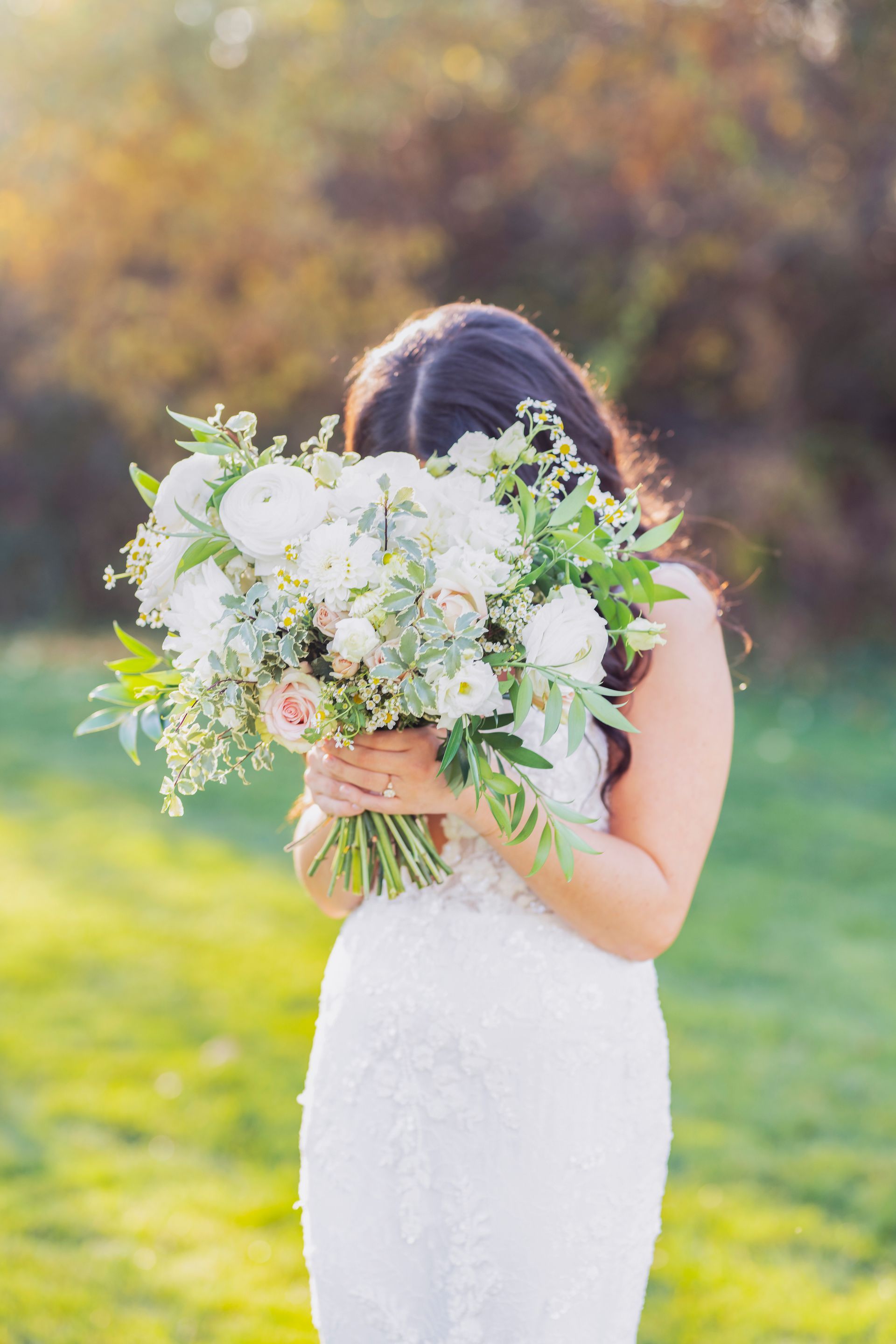 Bride in a white lace dress holding a large white-and-green bouquet outdoors