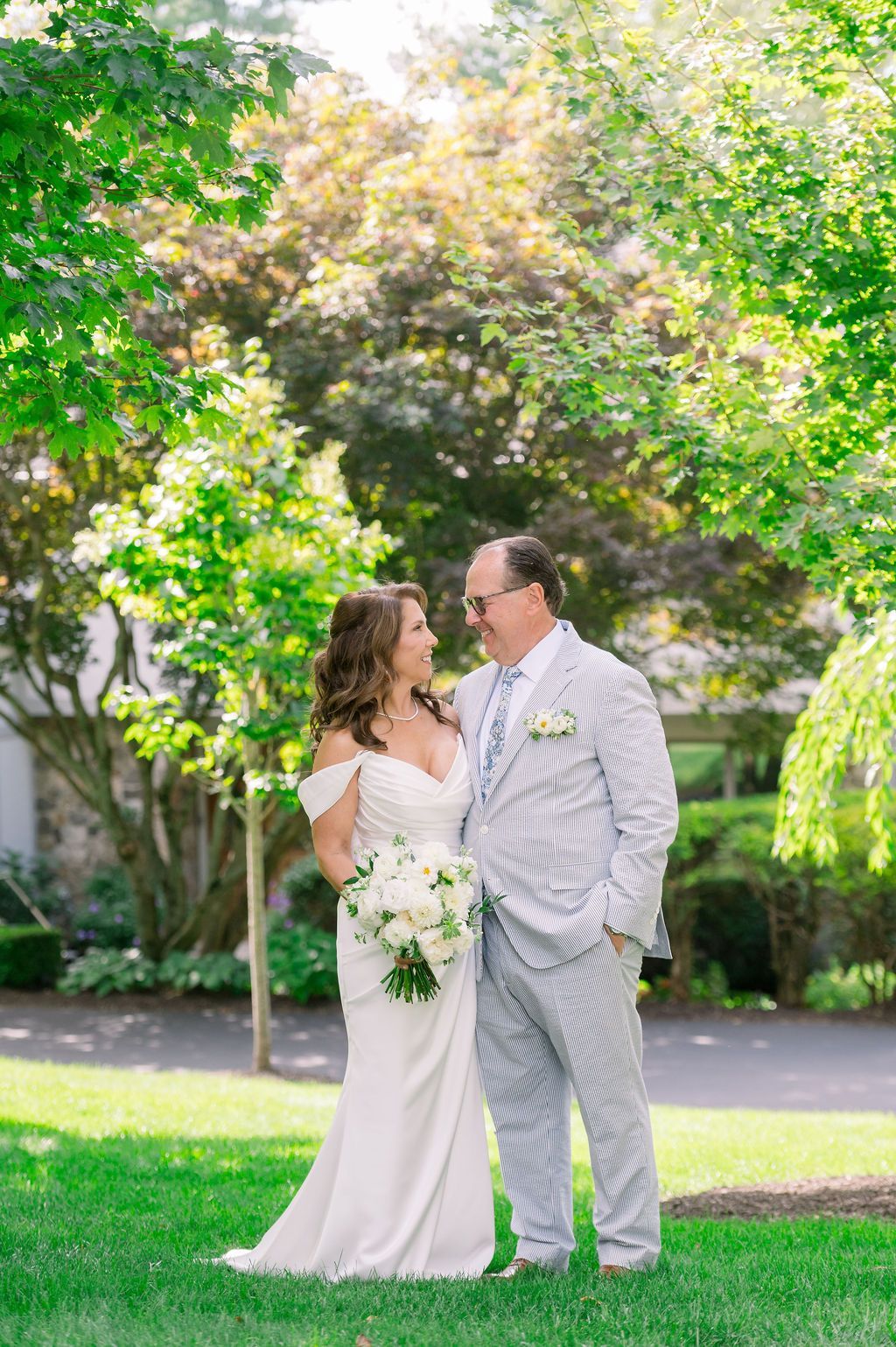 Wedding couple standing together in a garden, smiling and holding hands amid lush greenery.