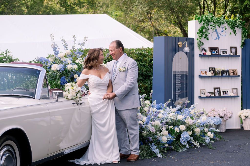 Bride and groom embracing beside a vintage white car and floral wedding backdrop outdoors