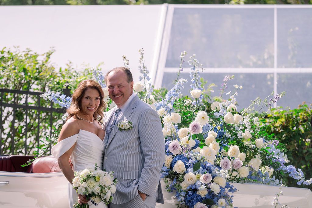 Couple in wedding attire posing beside a blue and white floral arrangement outdoors