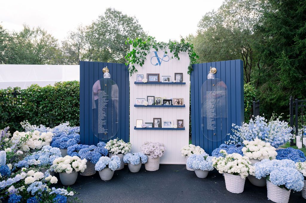Blue floral memorial display with white flowers, framed by navy panels and shelves outdoors