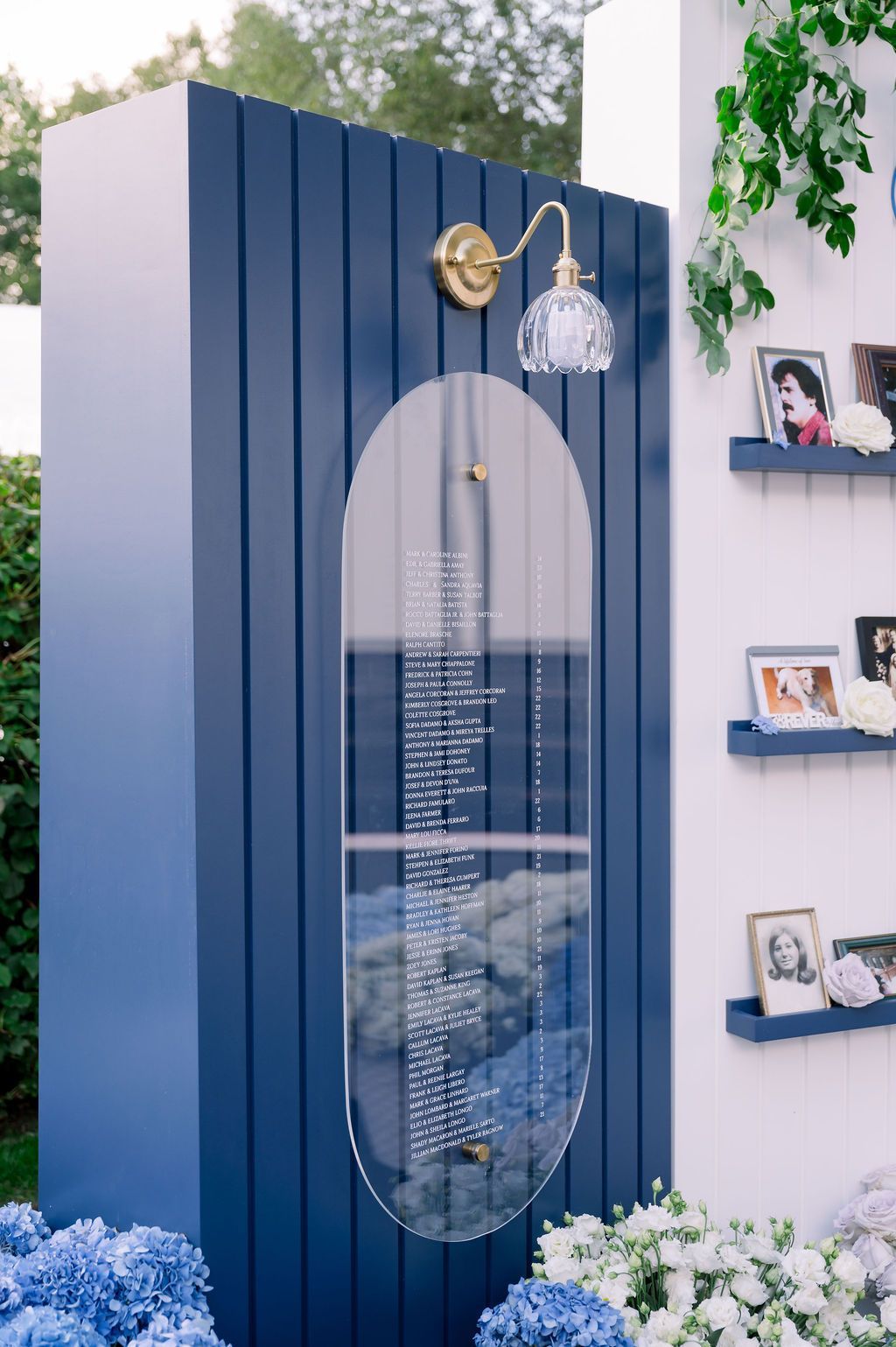 Blue decorative cabinet with an oval mirror panel, wall shelf photos, and white flowers in a garden-like display