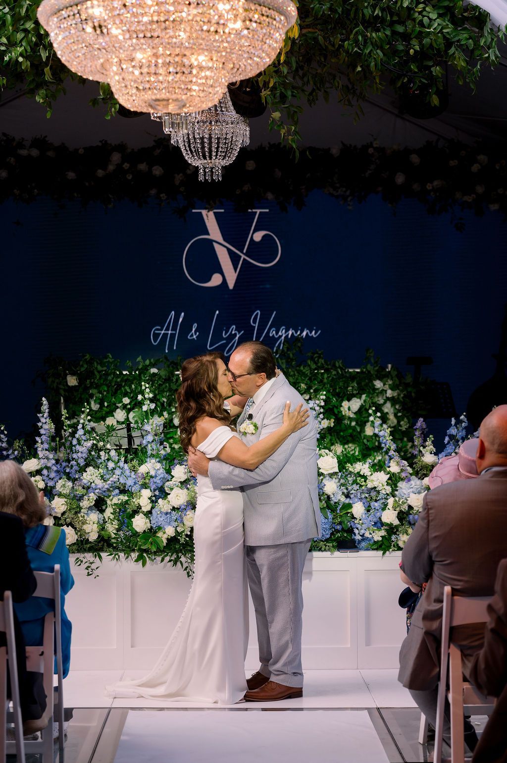 Bride and groom embracing at a wedding altar with white flowers and a chandelier overhead