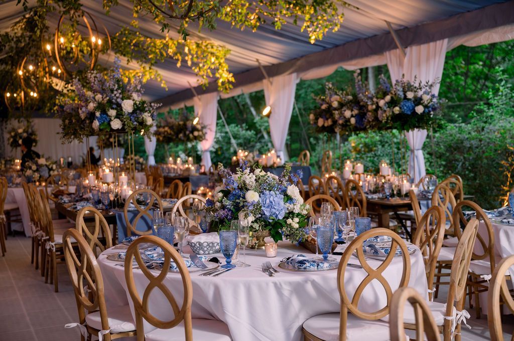Elegant outdoor wedding reception under a white tent with round tables, floral centerpieces, and warm string lights