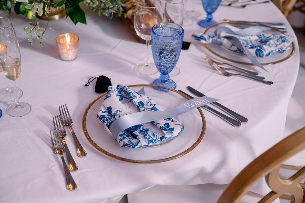 Elegant table setting with blue floral china, crystal glasses, gold-rimmed plates, and silverware on a white tablecloth