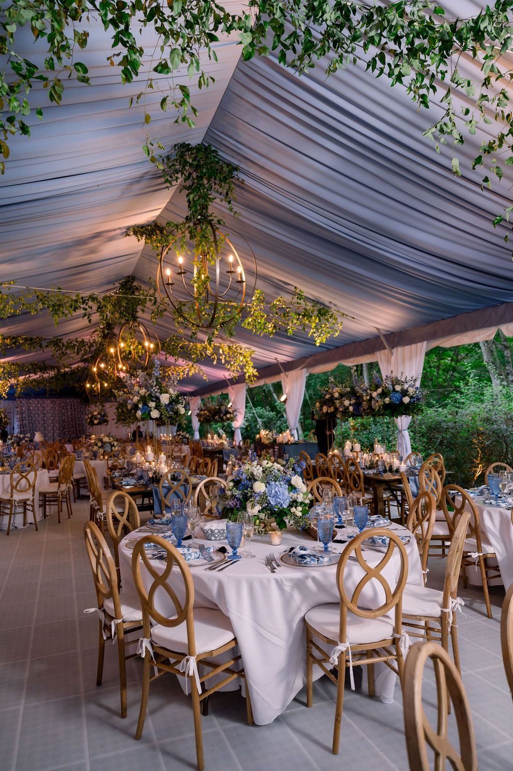 Elegant outdoor reception under a draped tent with white tablecloths, gold chairs, and floral centerpieces.