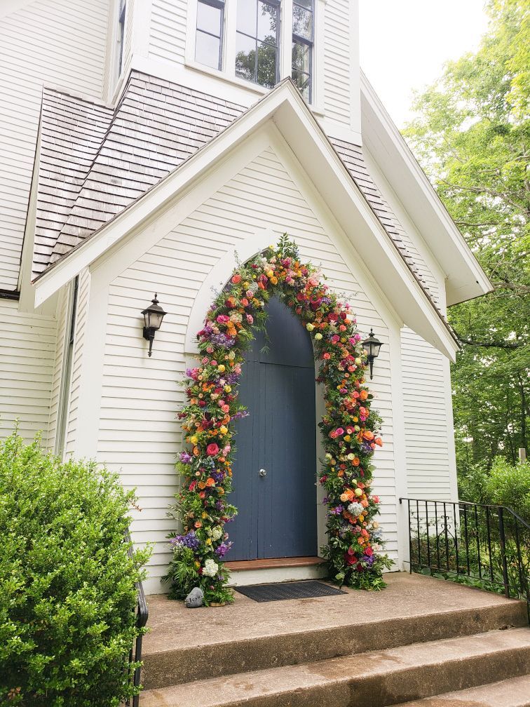 Flower-covered arched doorway on a white church building with steps and a blue door