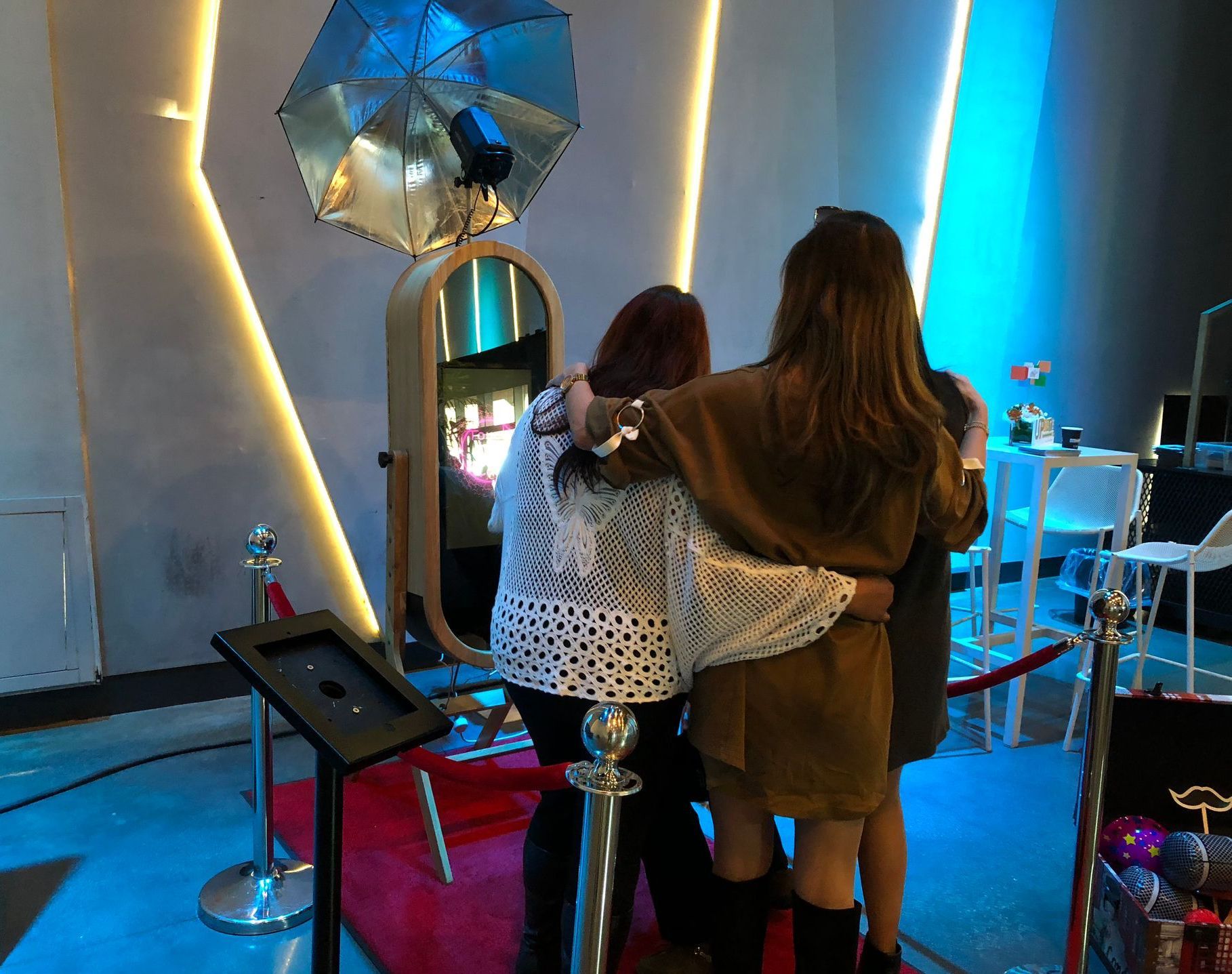 Two people stand arm in arm in a colorful indoor exhibit with neon lights and a reflective display.